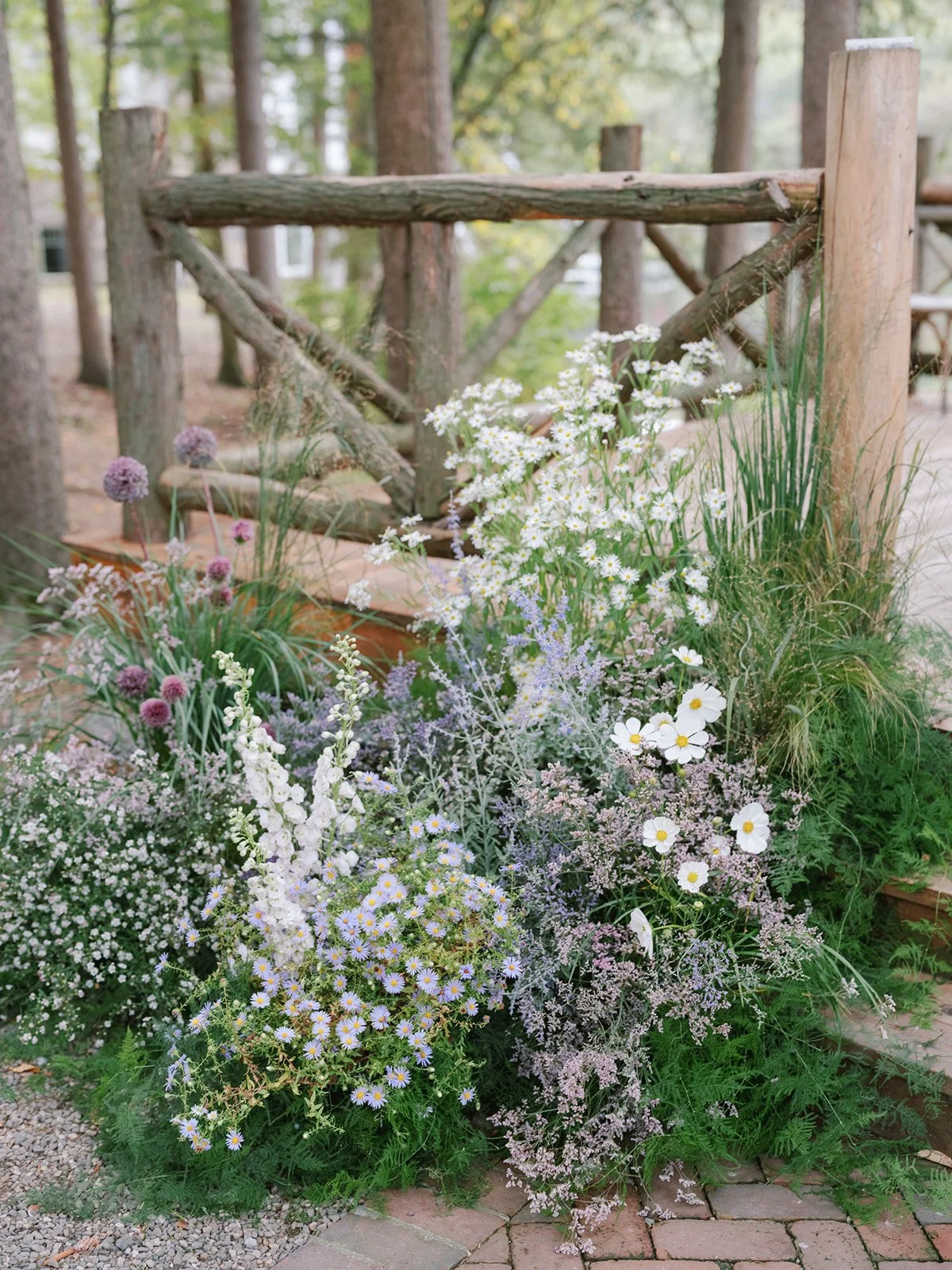 Colorful garden with white, purple, and pink flowers next to a wooden fence and brick pathway.