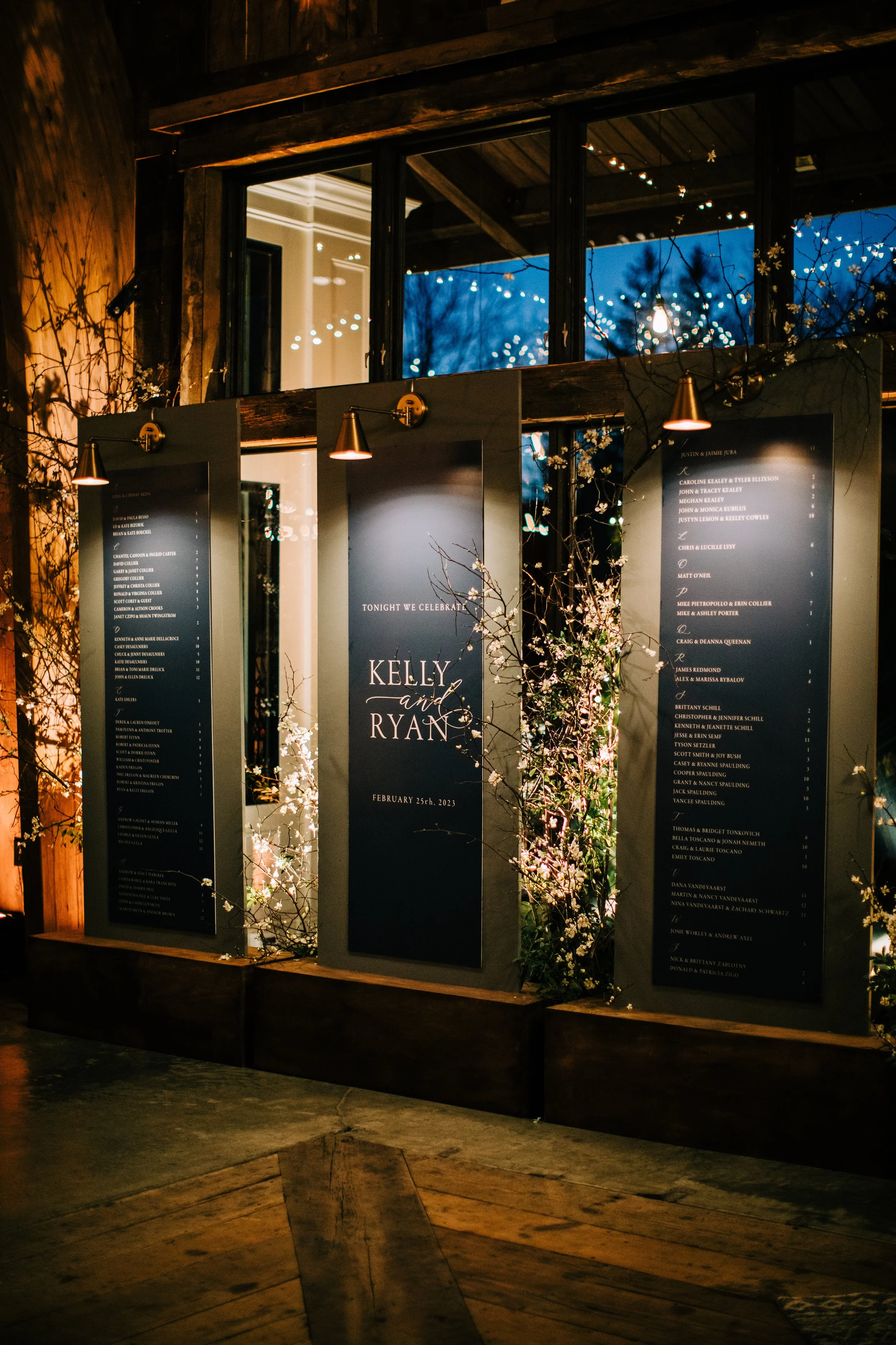 Wedding reception seating chart for Kelly and Ryan on February 25th, 2023, decorated with flowering branches and soft lighting.
