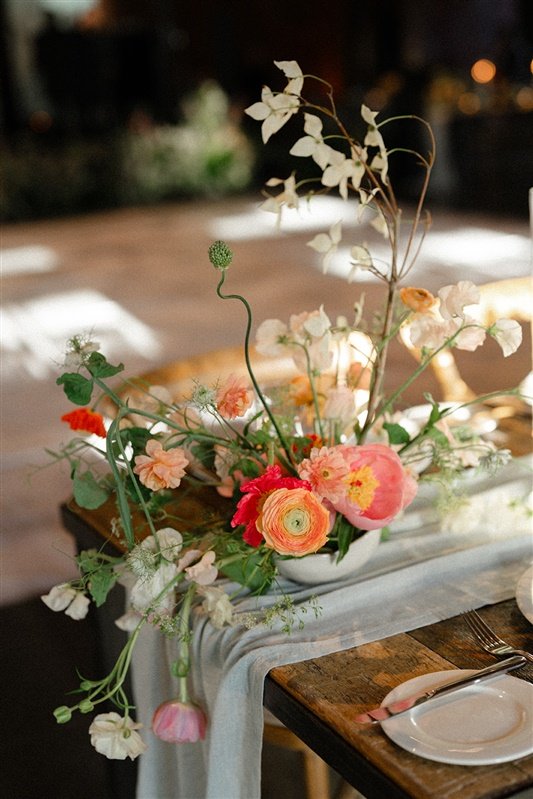 Elegant floral centerpiece with pink, white, and peach flowers on a table with plates and silverware.