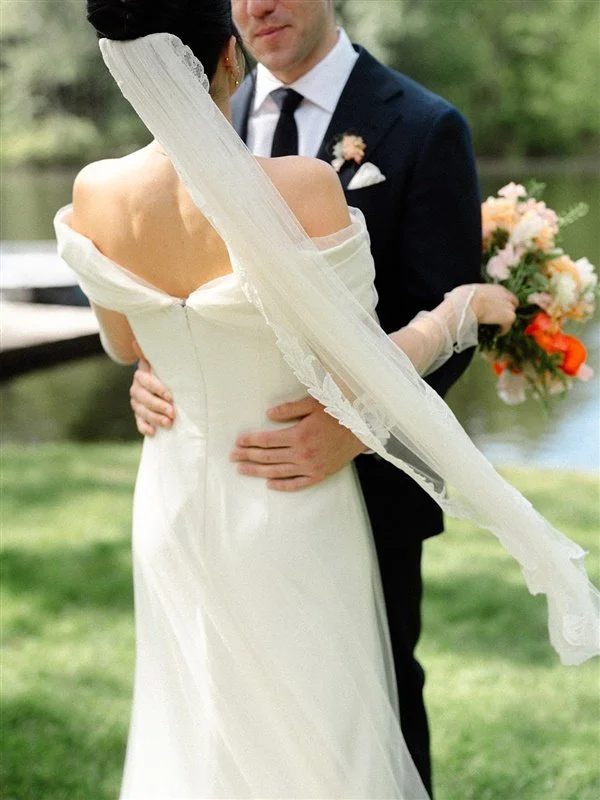 A bride and groom embrace outdoors, the bride holding a bouquet of flowers.