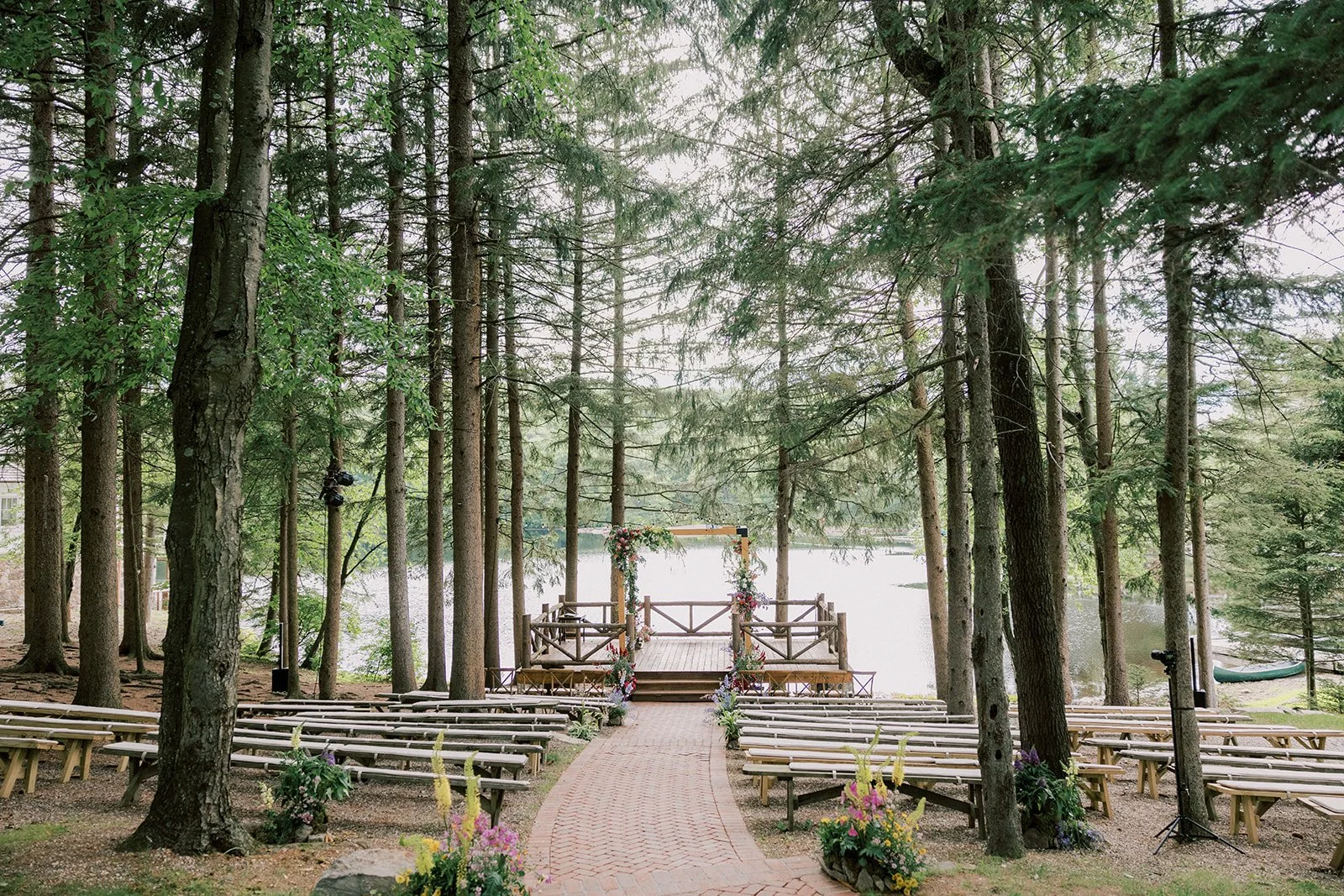 Outdoor wedding ceremony setup with benches, floral decorations, wooden arch, and lake view surrounded by trees