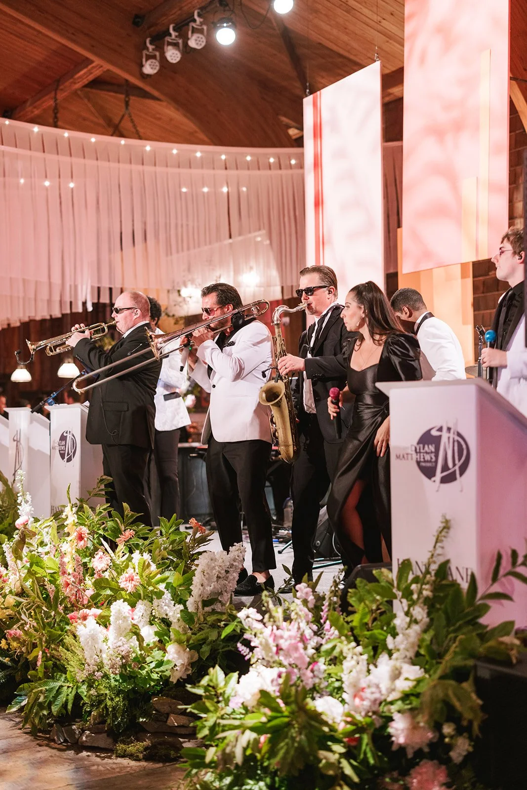 Musicians performing on stage at a formal event with floral arrangements and decorative lighting.