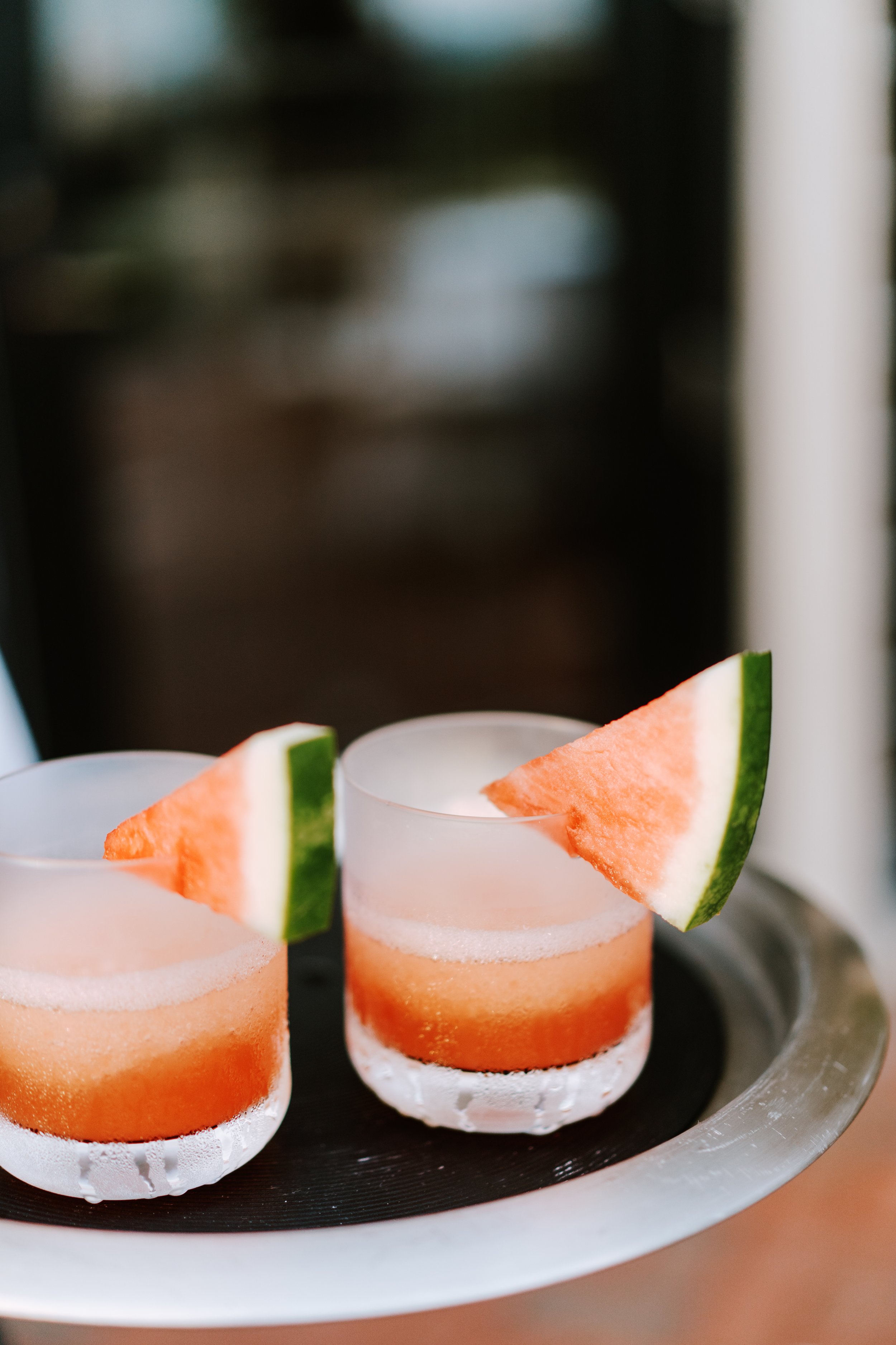 Two glasses of watermelon cocktail garnished with watermelon and lime slices on a tray.