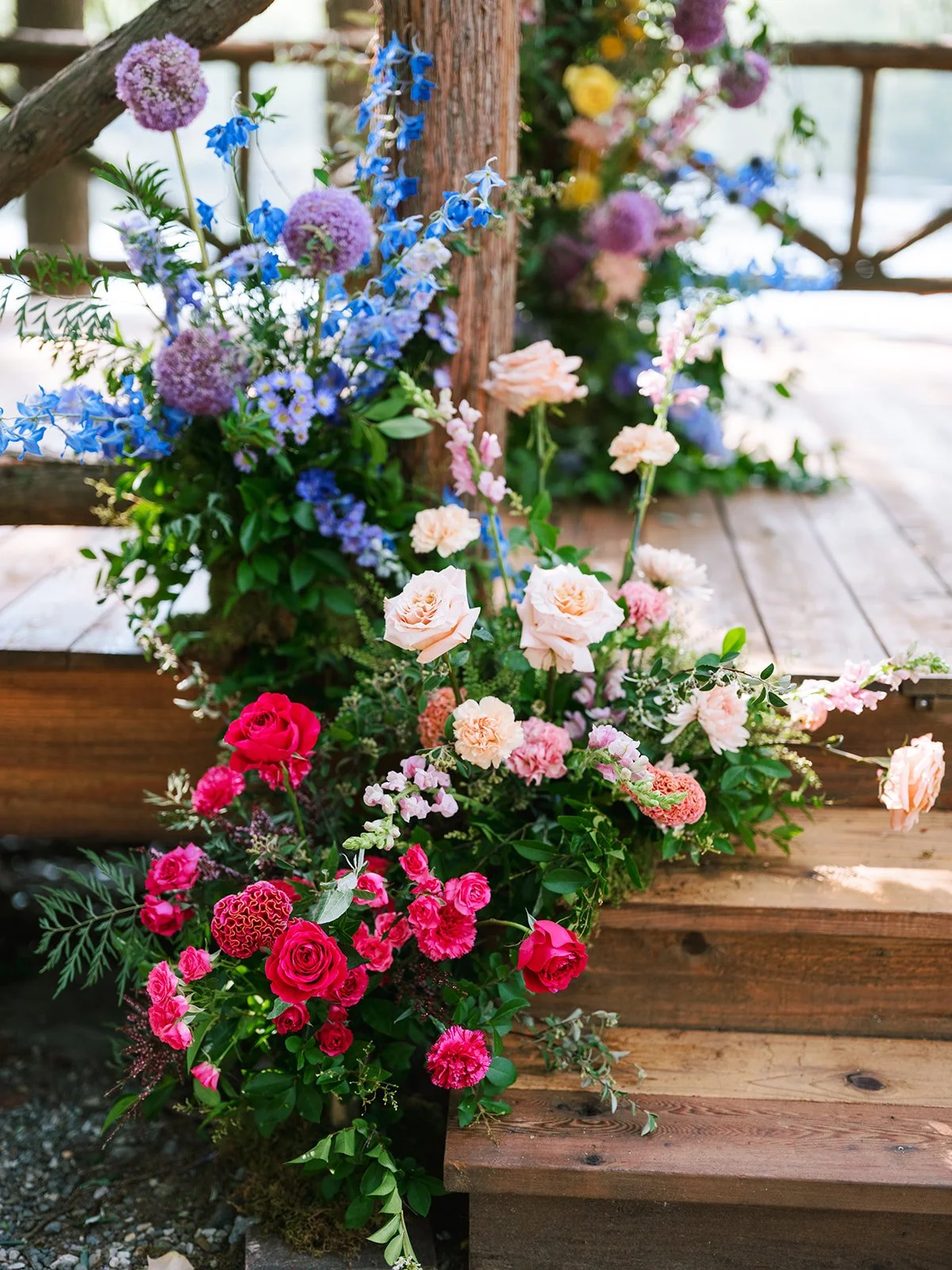 Colorful flower arrangement with pink, blue, and purple flowers on a wooden bridge.