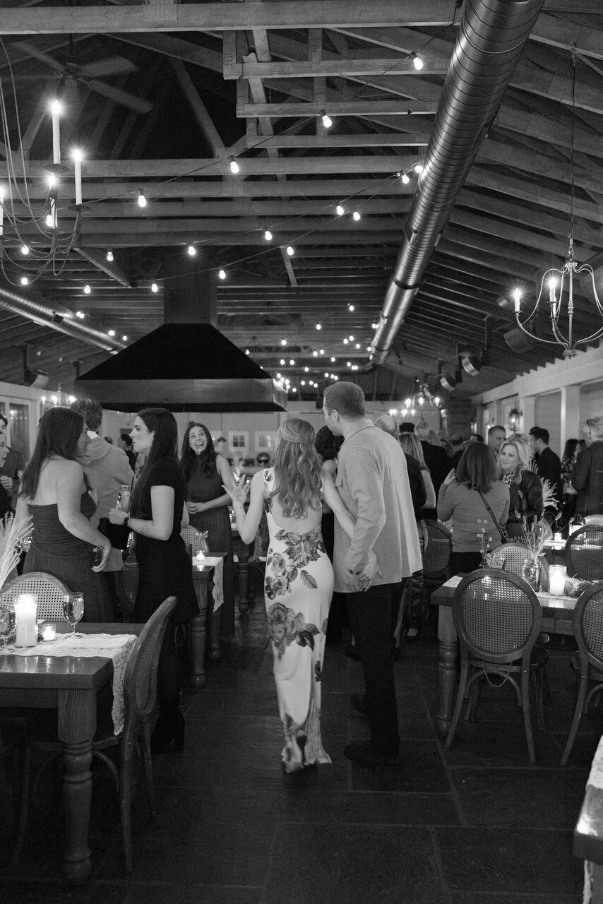 People socializing and dancing in a lively, decorated indoor venue with string lights and chandeliers.