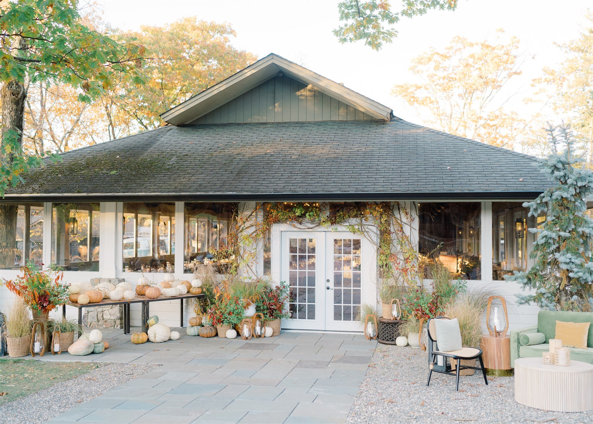 Exterior of a building decorated for fall with pumpkins, gourds, and autumn foliage outside and comfortable seating near the entrance.