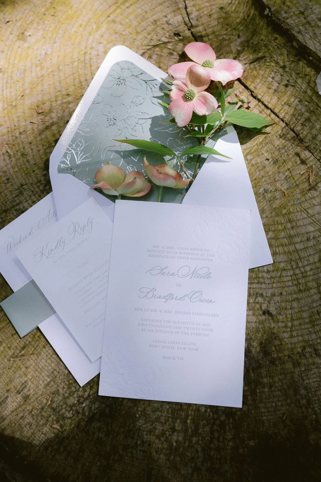Wedding invitation with pink flowers and petals, placed on a wooden surface.