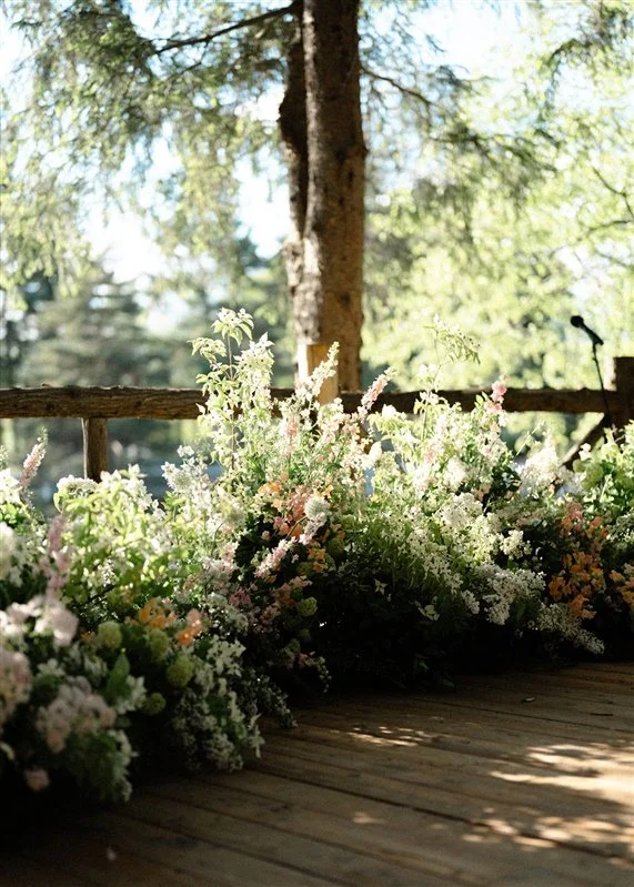 Flower arrangements on a wooden deck with trees in the background.