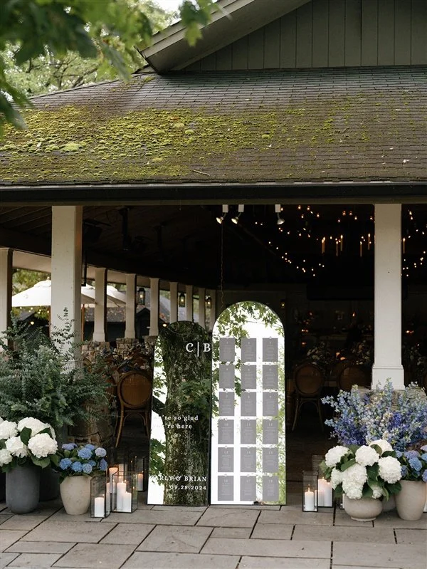 Decorative mirror boards with greenery, white flowers, and candles at a wedding reception entrance.
