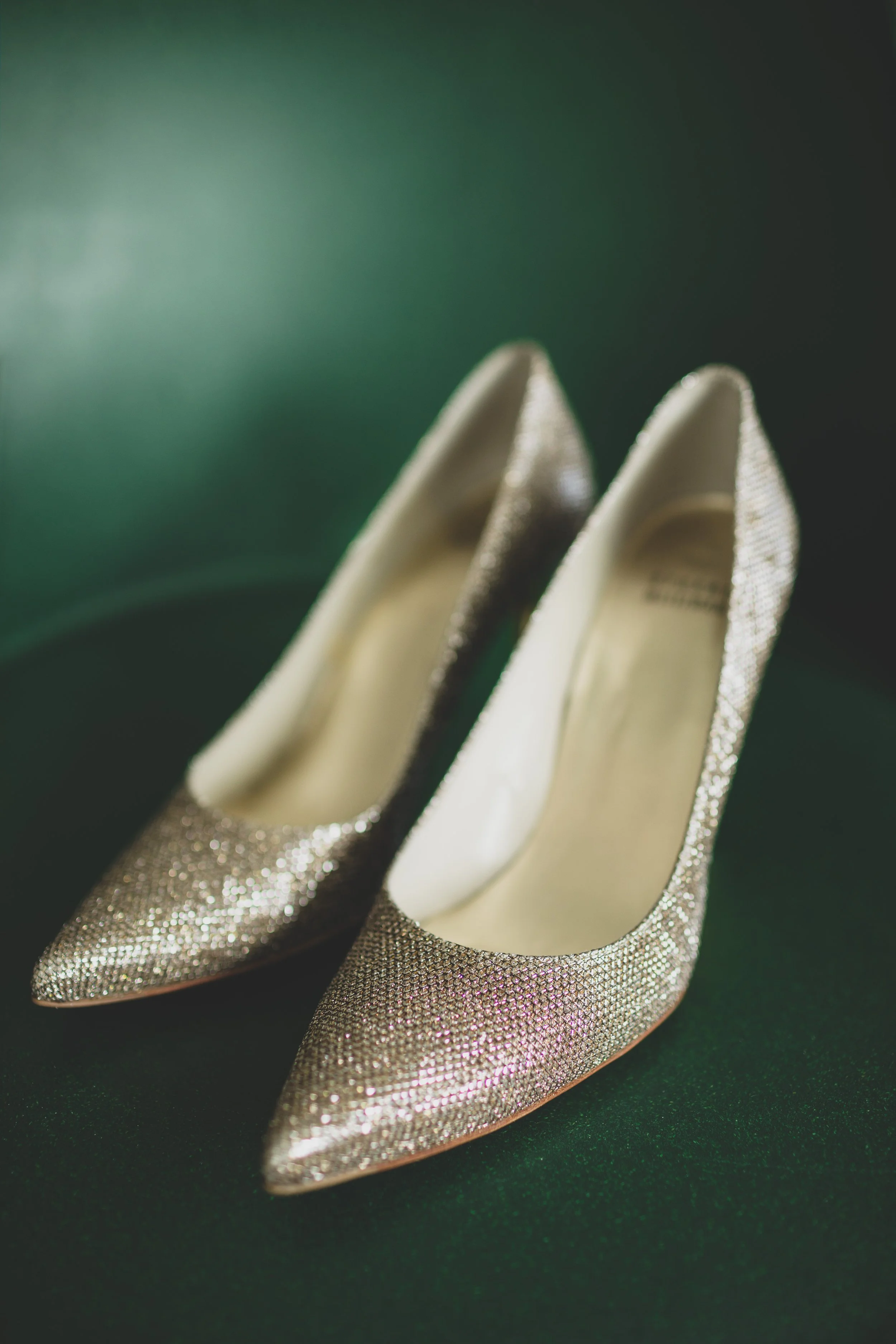 A pair of sparkling high-heeled shoes with pointed toes, decorated with glittery rhinestones, resting on a dark green surface.