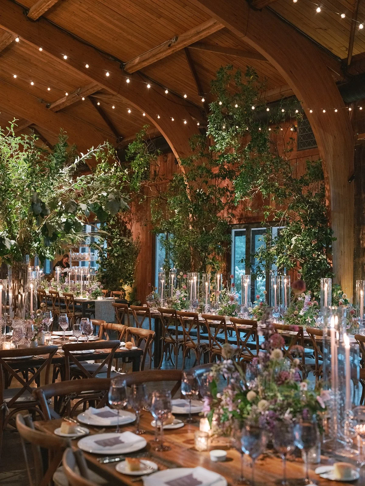 Elegant indoor wedding reception decorated with flowers, candles, and string lights, featuring a long dining table with chairs.