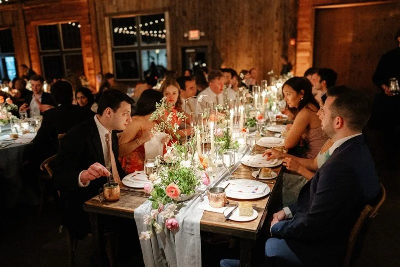 A formal dinner party with guests seated around a long decorated table in a wooden event space.