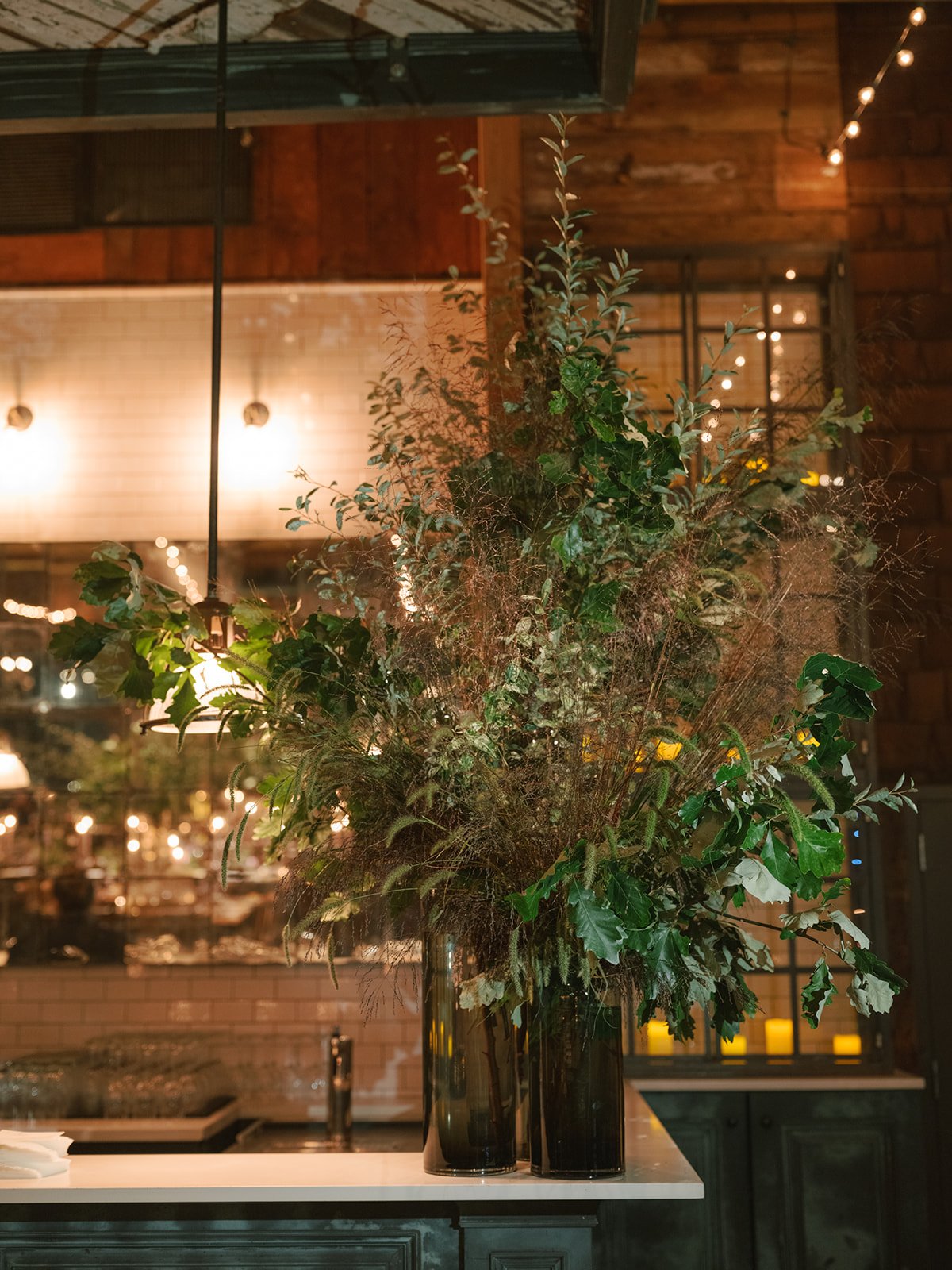A large floral arrangement with greenery in tall glass vases on a white countertop in a warmly lit indoor space.