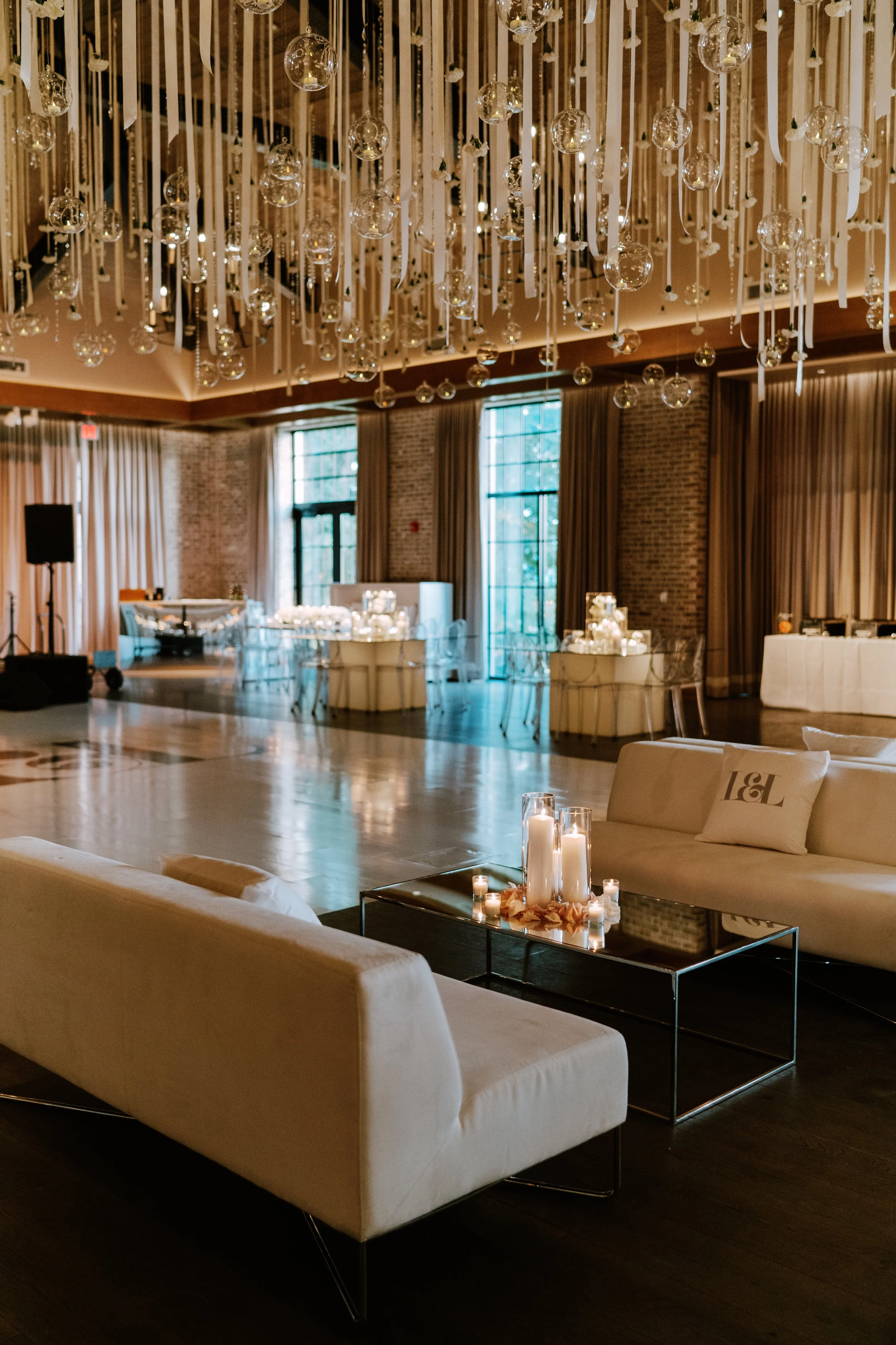 Elegant event space decorated with hanging glass orbs and ribbons, tables set with candles, and comfortable seating.