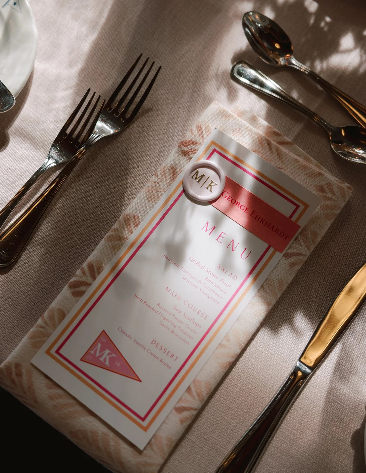 A restaurant place setting with a menu on a beige tablecloth, silverware including forks and spoons, and a small round badge on the menu.
