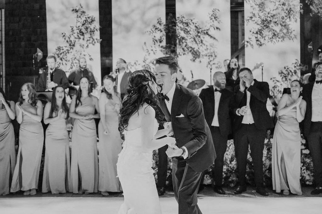 A wedding dance with the bride and groom in the center, surrounded by bridesmaids and groomsmen, and a band performing in the background.