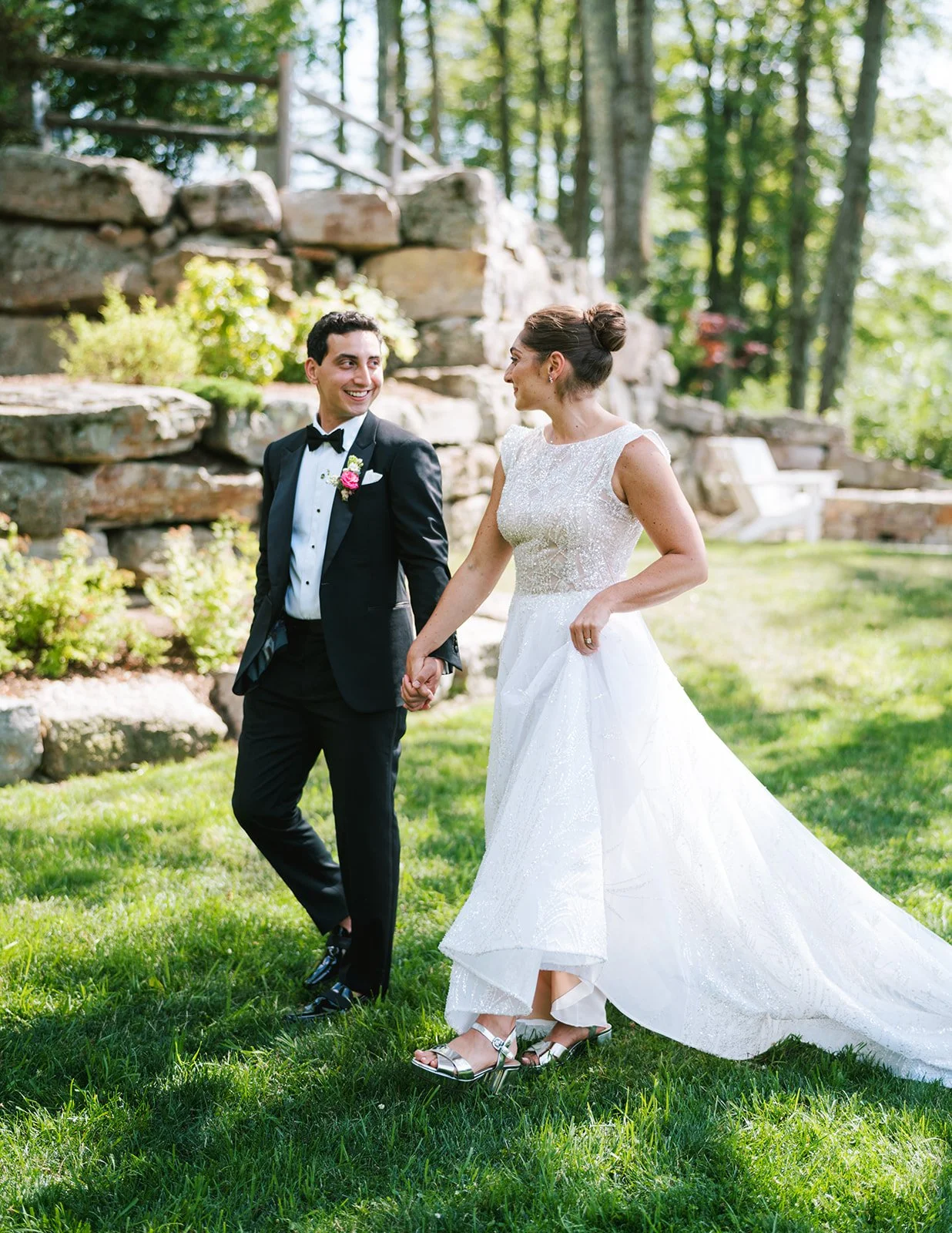 A bride and groom holding hands outside in a lush green garden, smiling at each other.
