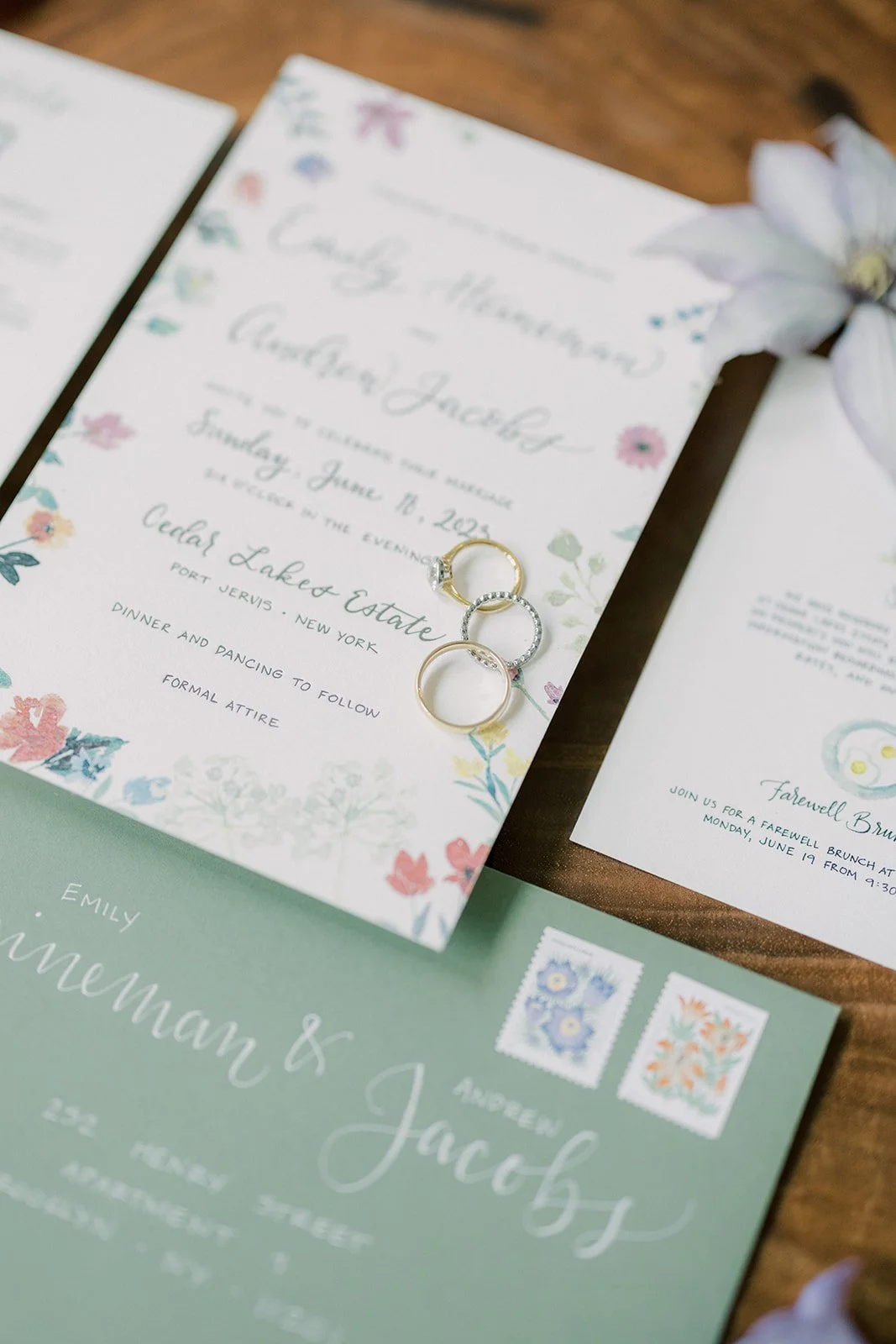 A wedding invitation and RSVP card featuring floral designs, with three rings placed on the invitation. There is also an envelope with the recipient's name and address.
