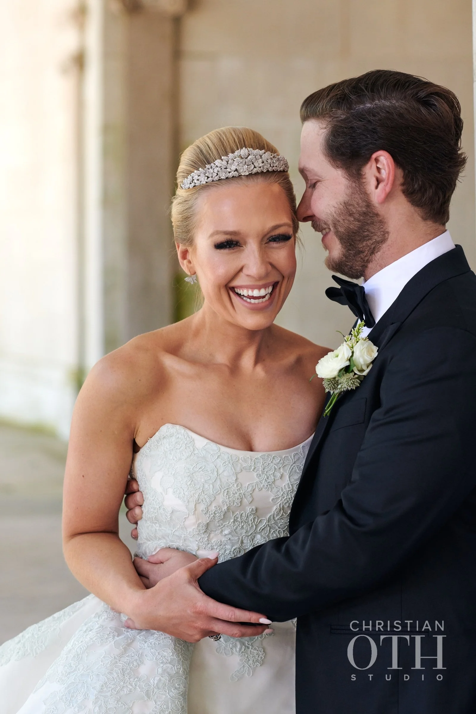 A happy bride and groom sharing a joyful moment on their wedding day, smiling and holding each other in an outdoor setting with neutral background.