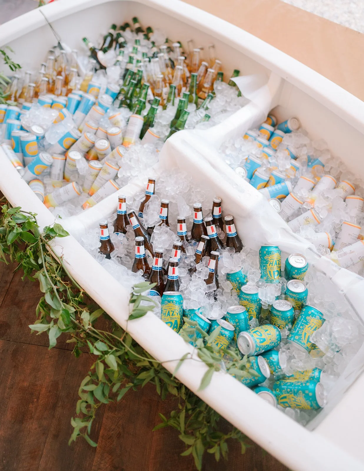 Ice-filled cooler containing bottles and cans of soda and beer, decorated with green leaves.