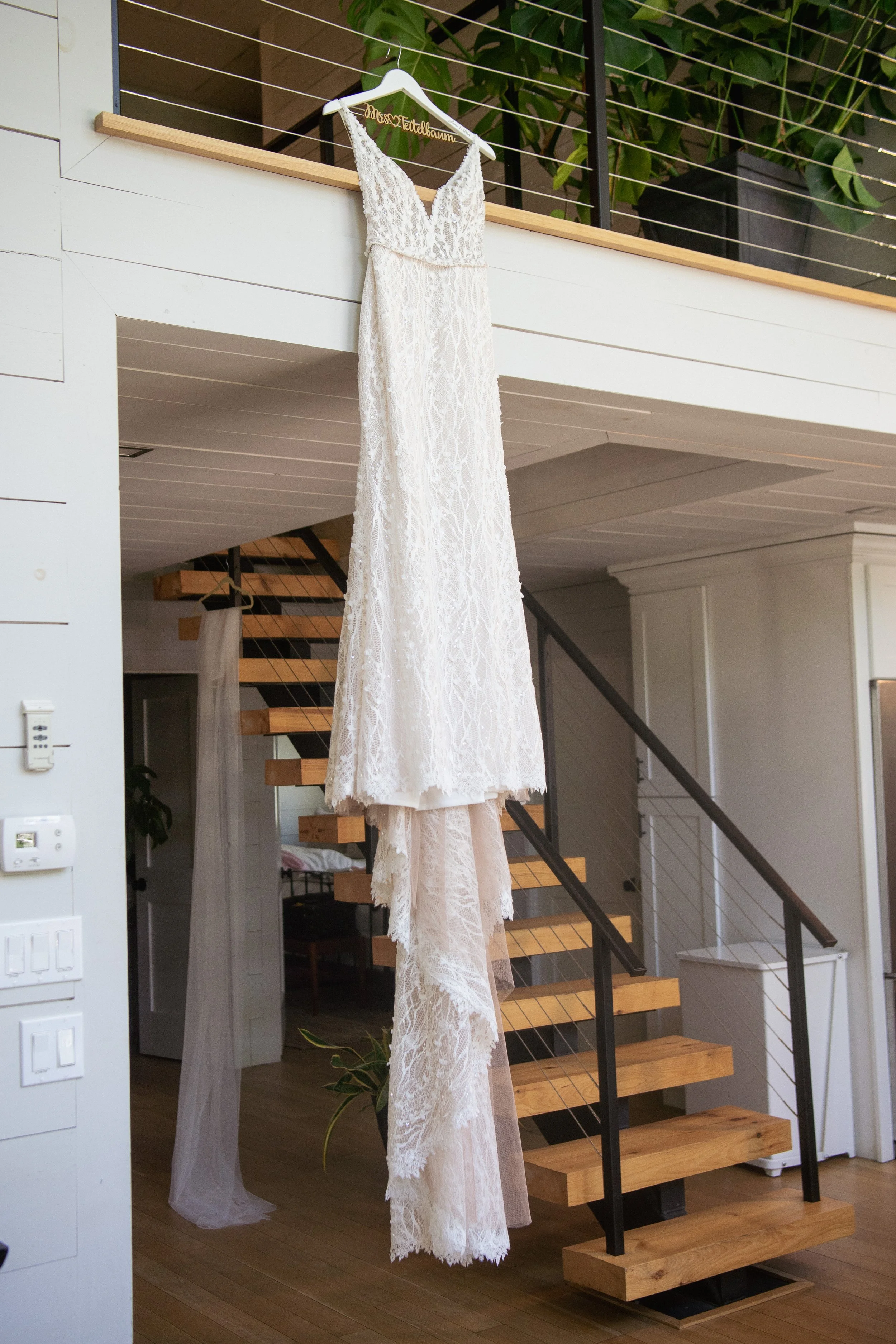 A white lace wedding dress hanging on a hanger from a loft railing in a modern home interior.