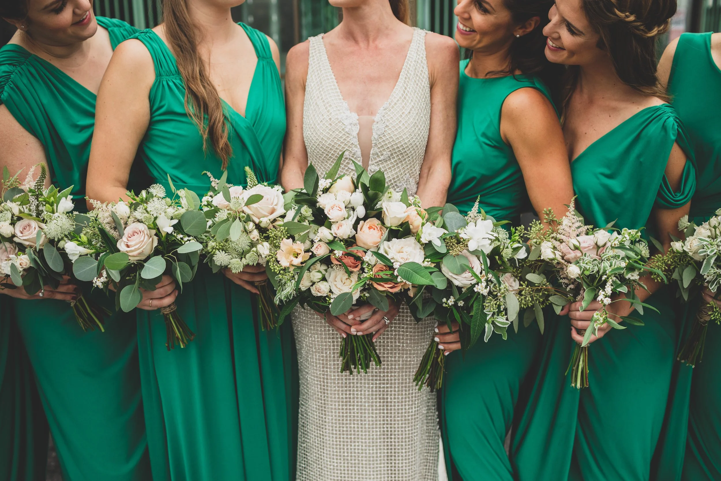 A group of women in green dresses holding bouquets of flowers at a wedding.
