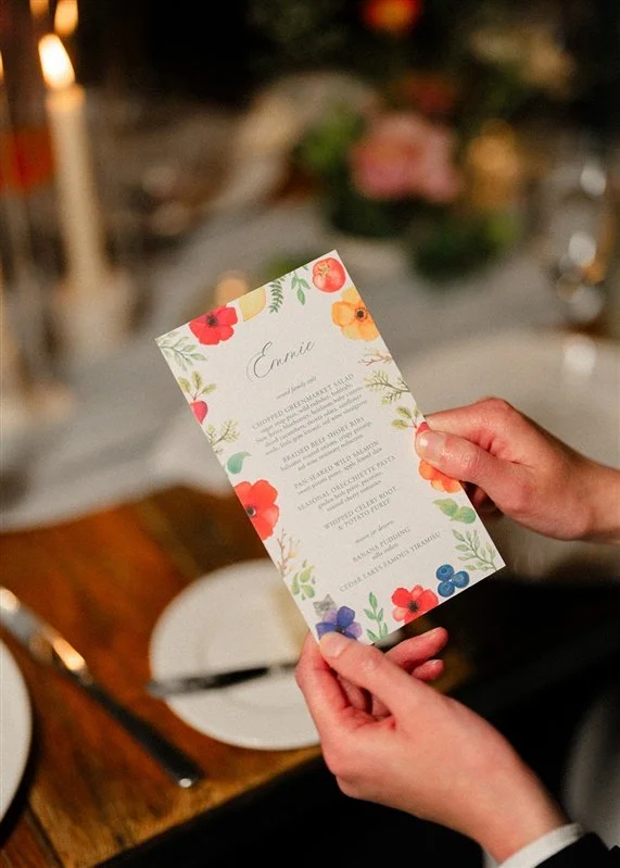 Person holding a floral-designed menu card at a dining table.