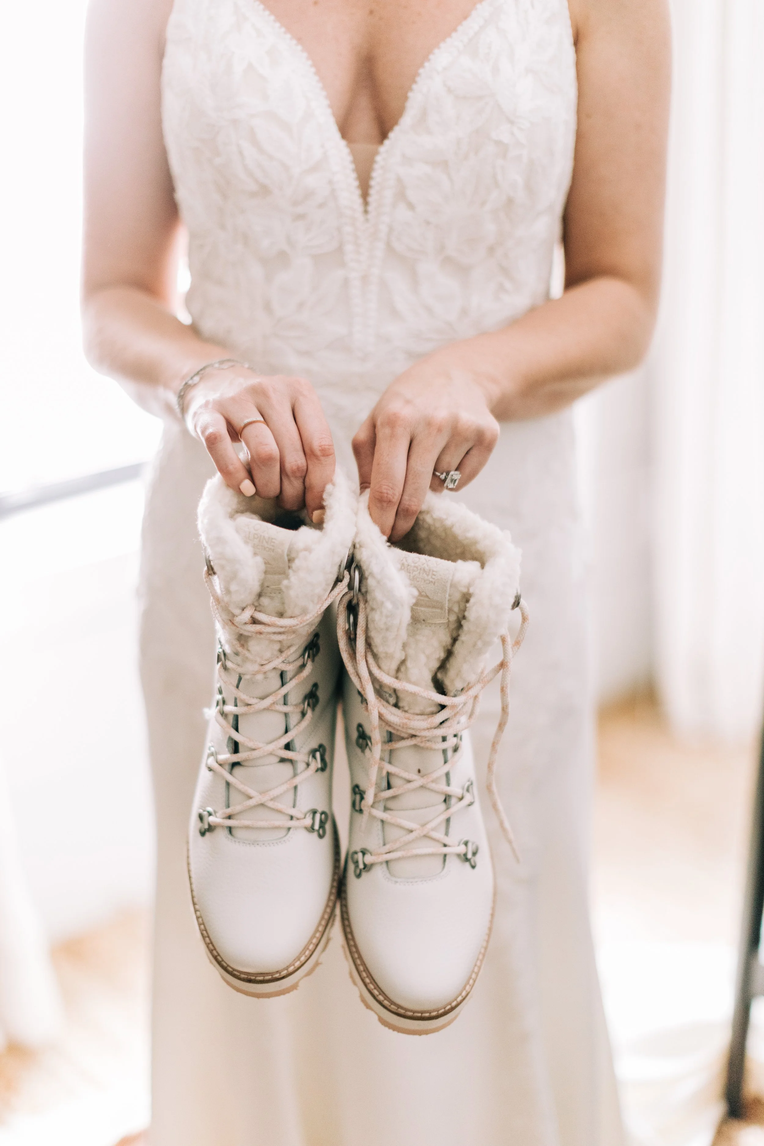 A woman in a white wedding dress holding a pair of white fur-lined winter boots.