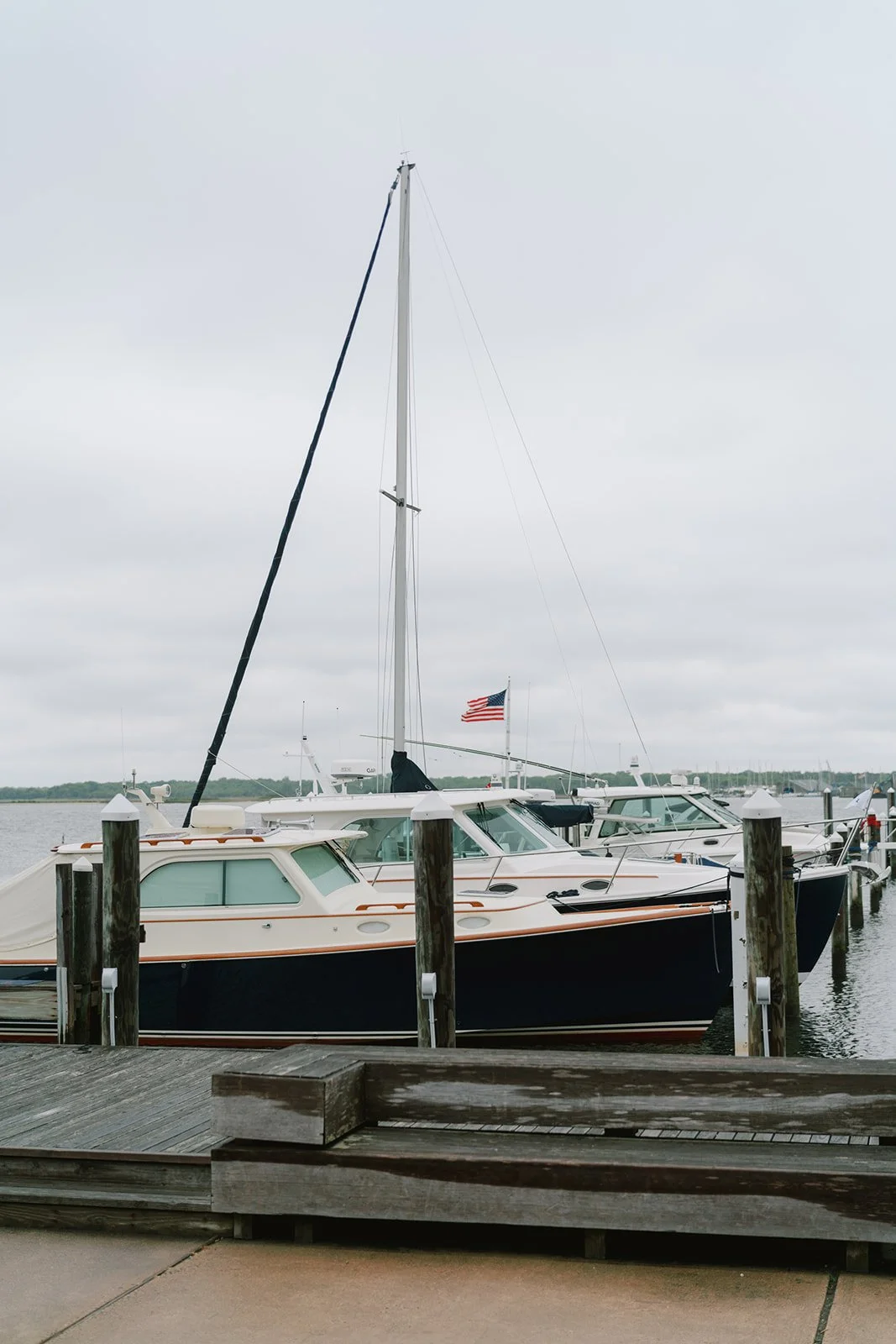 Several boats docked at a marina on a cloudy day, with a visible American flag on one of the boats.