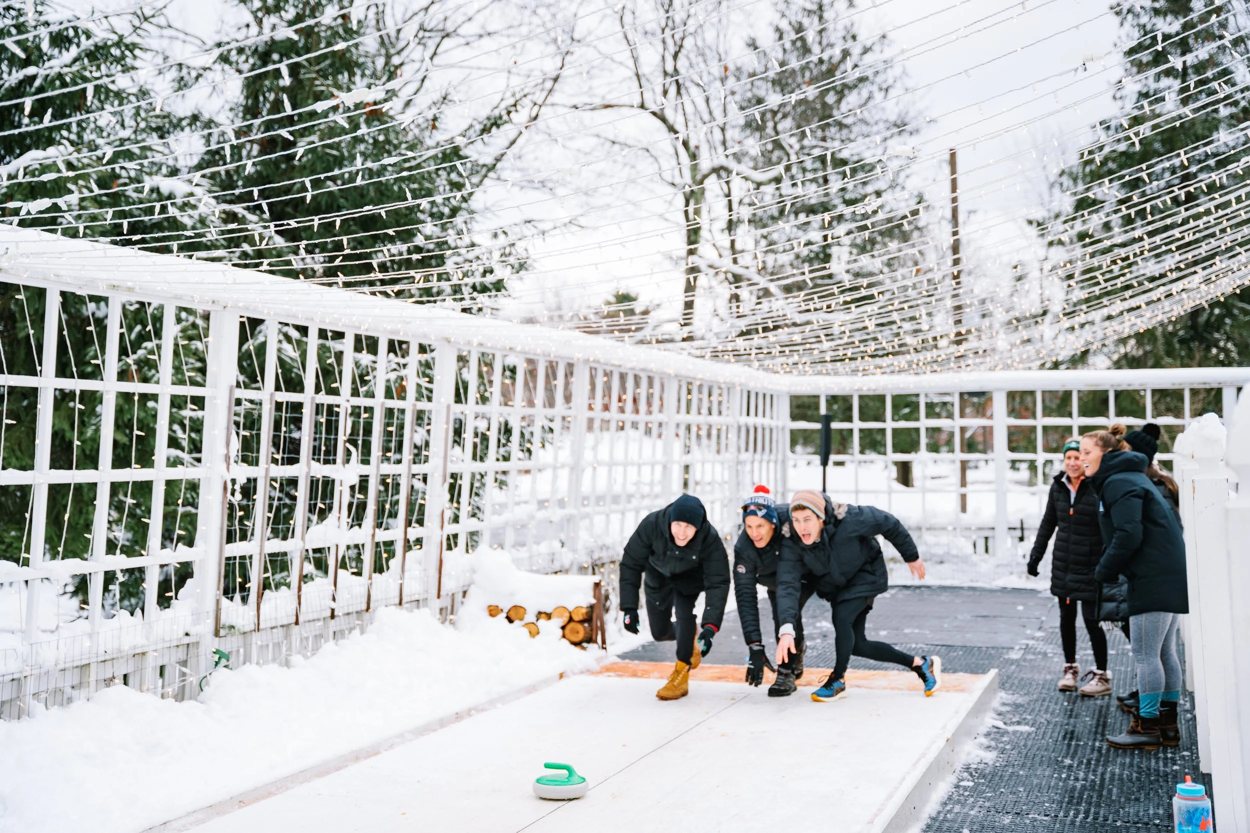 People playing curling outdoors in a snowy environment.