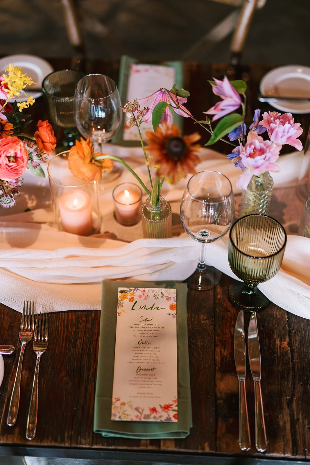 A decorated table set for a special occasion with flowers, candles, wine glasses, and a menu card.