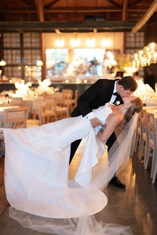 A newlywed couple sharing a romantic dance in a decorated wedding reception hall with warm lighting.