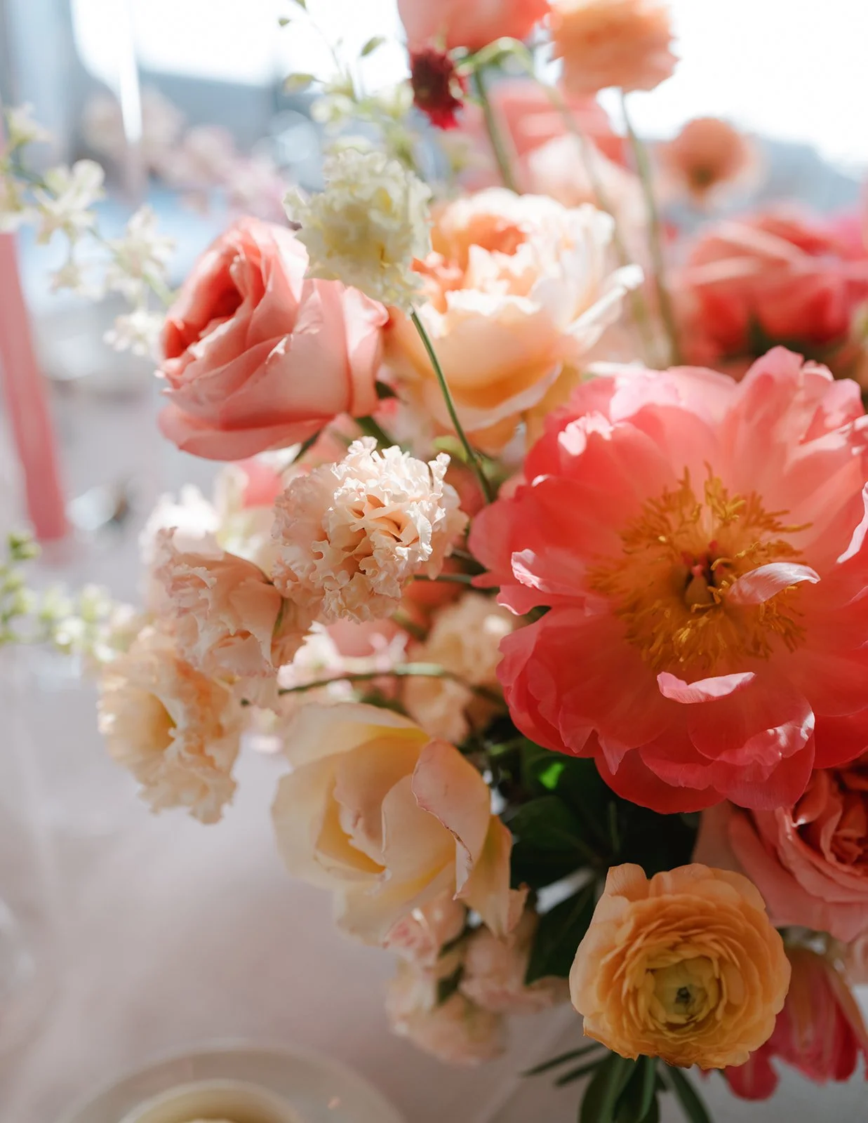 Close-up of a bouquet of pink, peach, cream, and white flowers with soft sunlight.