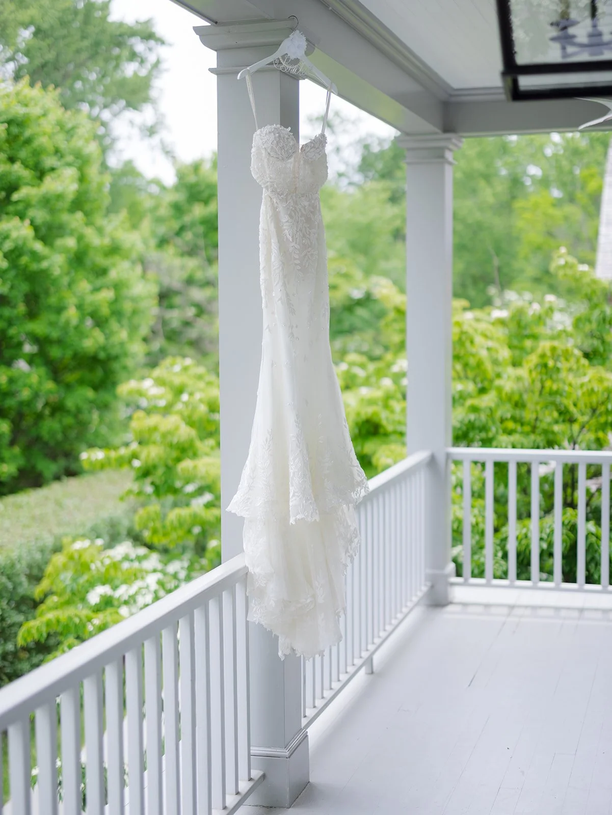Wedding dress hanging on a porch ceiling with a green garden background.