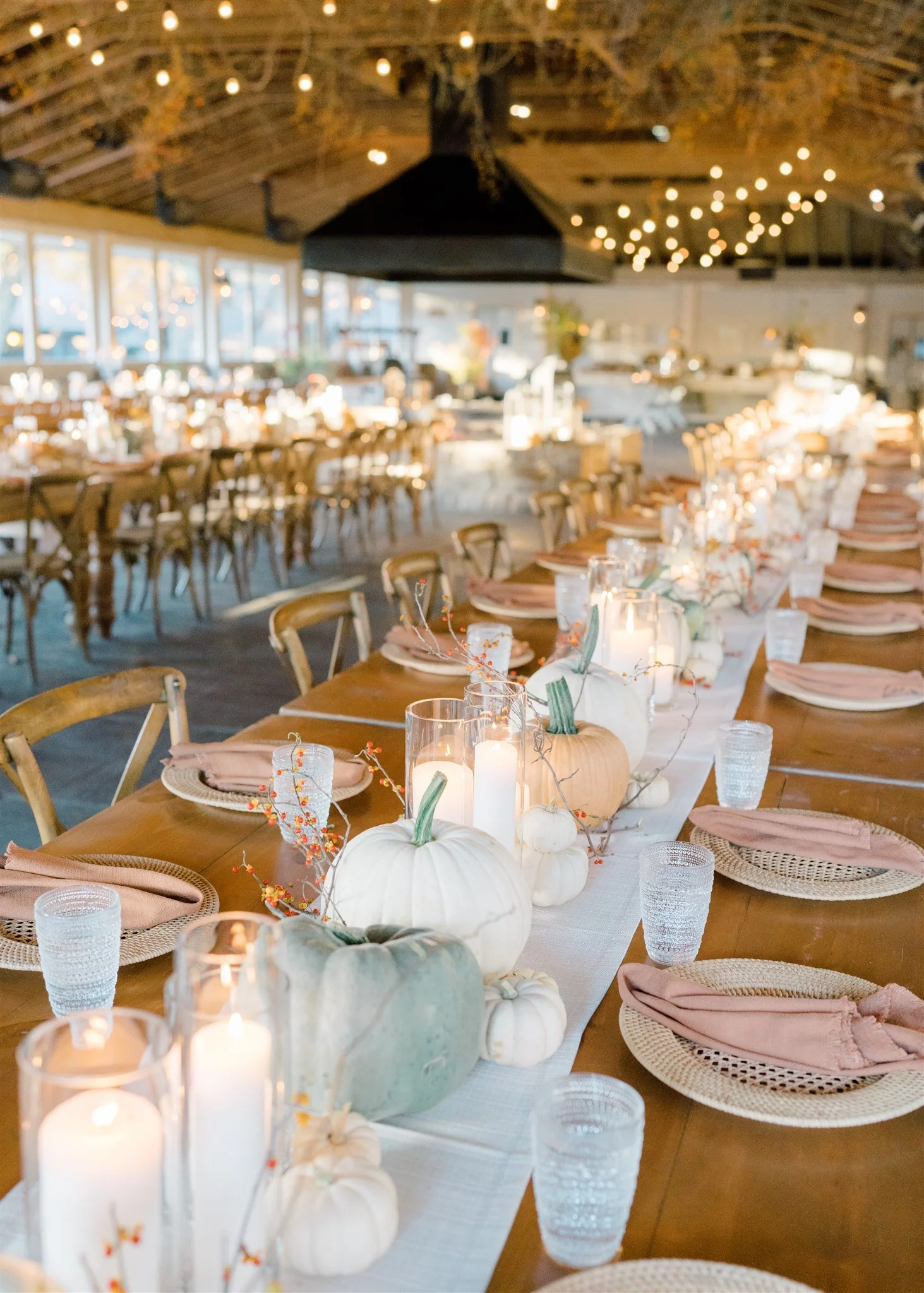 A decorated indoor dining table with pumpkins, candles, and fall-themed accents, set with plates, glasses, and napkins for a festive event.