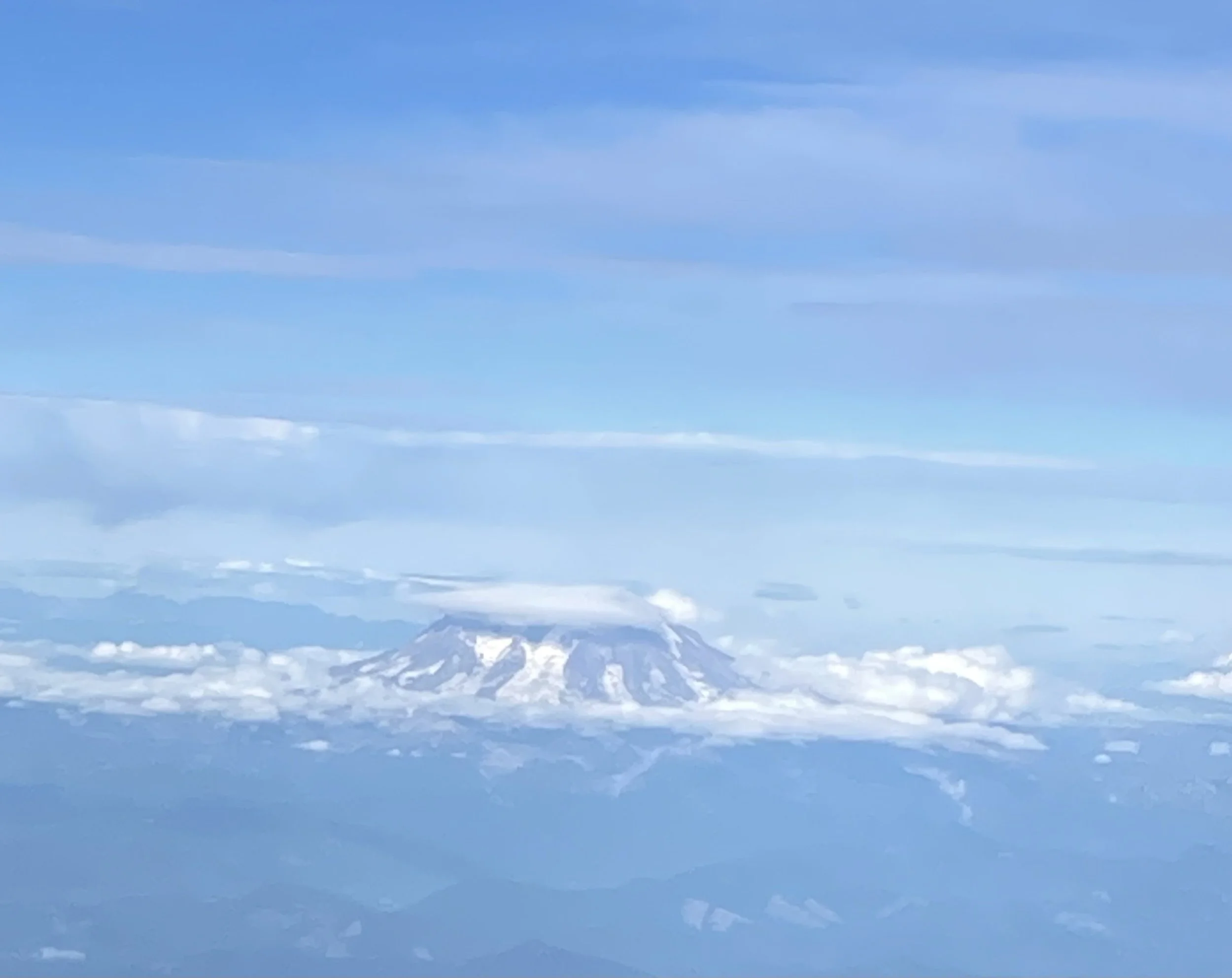Mountain peak covered in snow with a clear blue sky and wispy clouds above.
