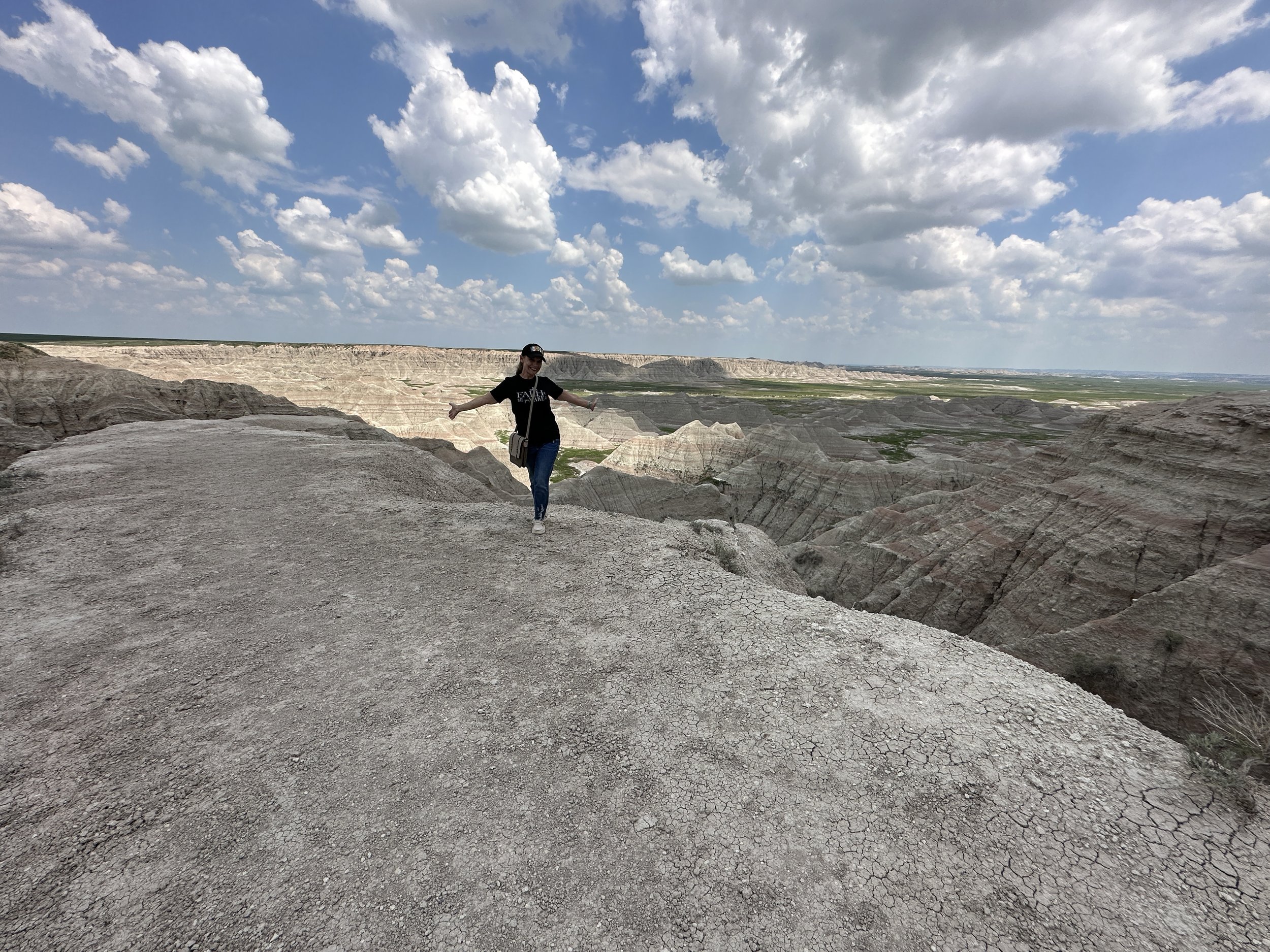 A person standing on a rocky ledge with a canyon landscape behind them, under a partly cloudy sky.