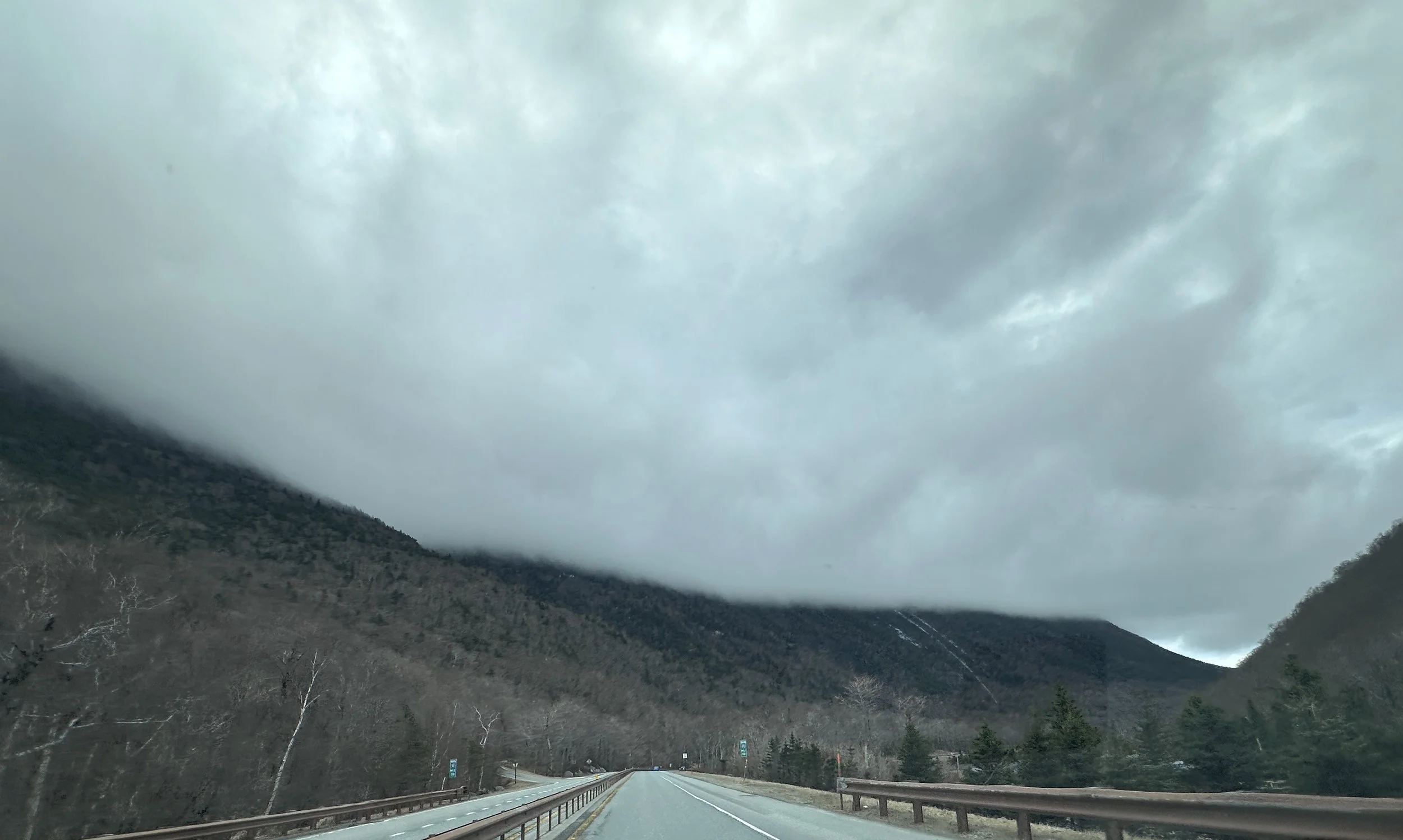 A scenic mountain landscape with a highway driving through the valley, surrounded by trees, during cloudy weather.