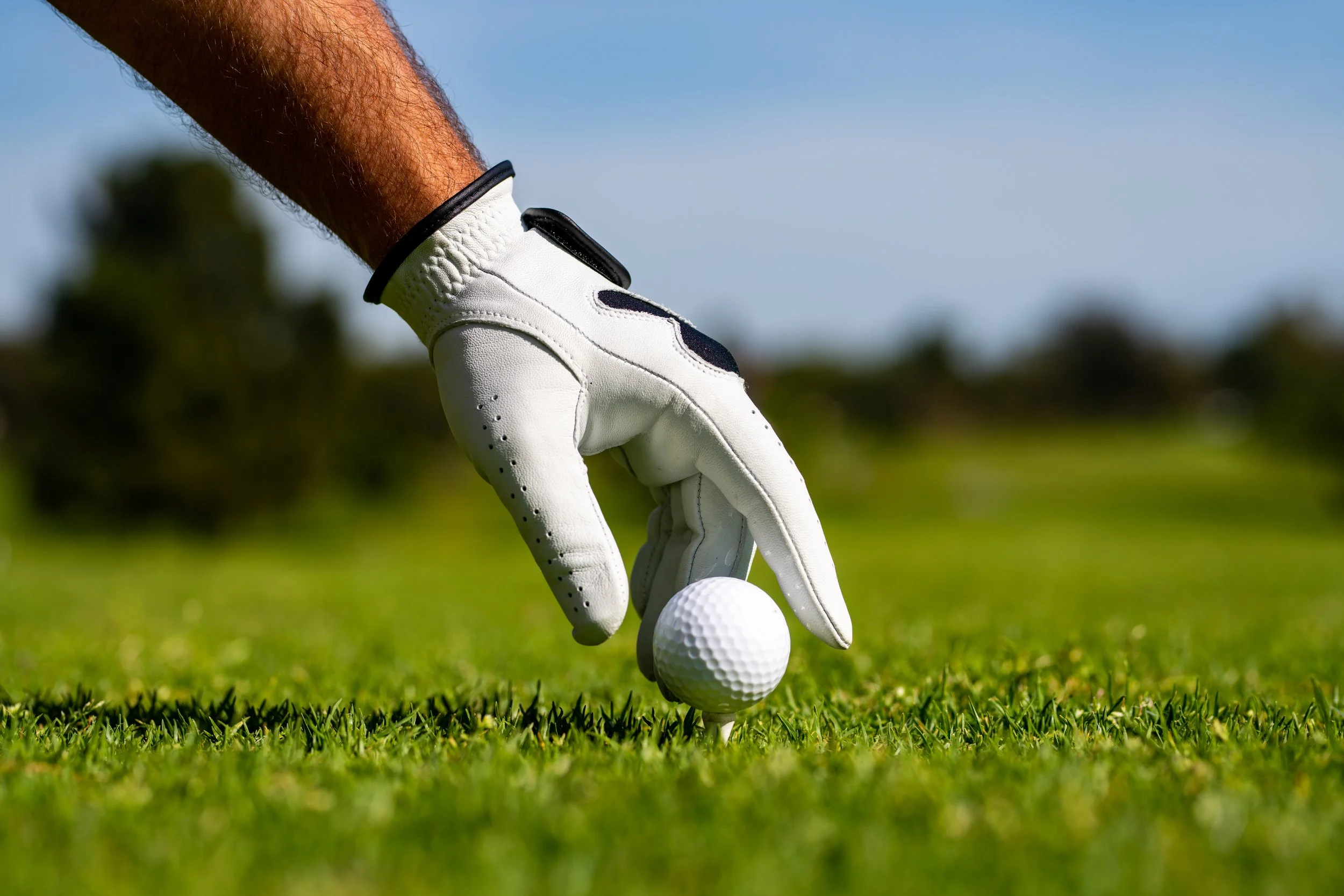 A person's hand wearing a golf glove placing a golf ball on a tee on a golf course.