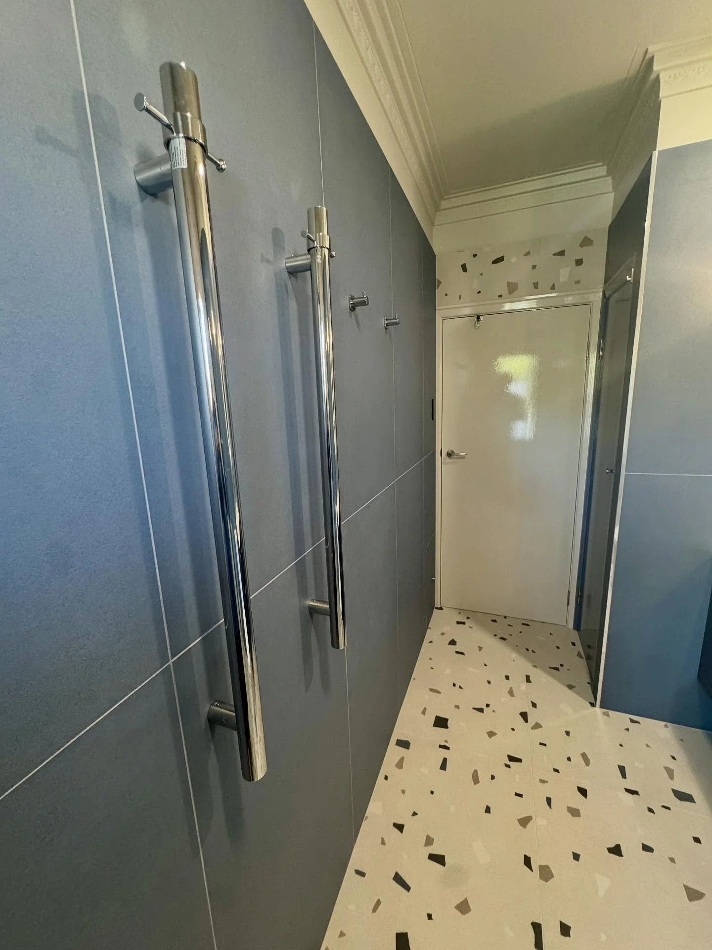 A hallway with blue wall panels, stainless steel handrails, and a terrazzo floor.