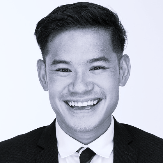 Black and white headshot of a smiling young man in a suit and tie against a plain background.