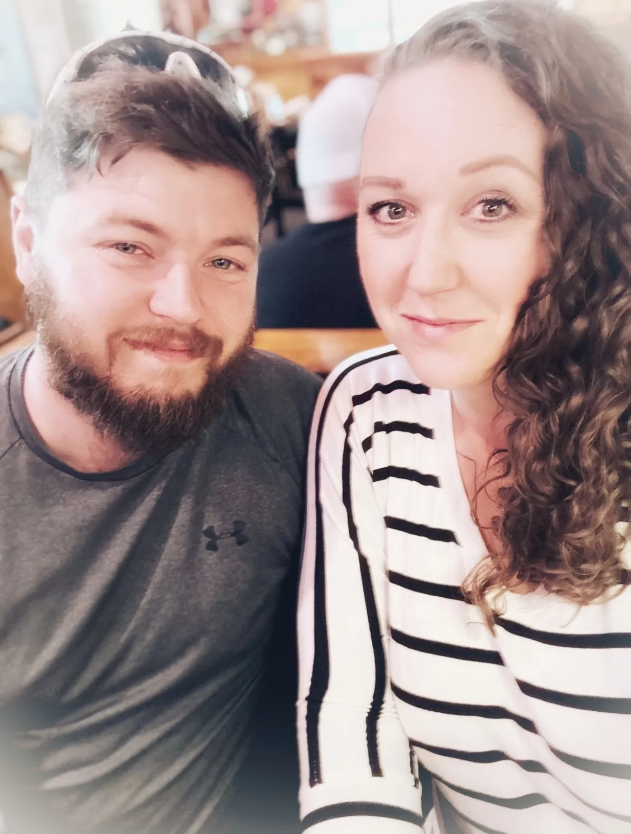 A man with a beard and a woman with curly hair sitting together at a restaurant, smiling at the camera.