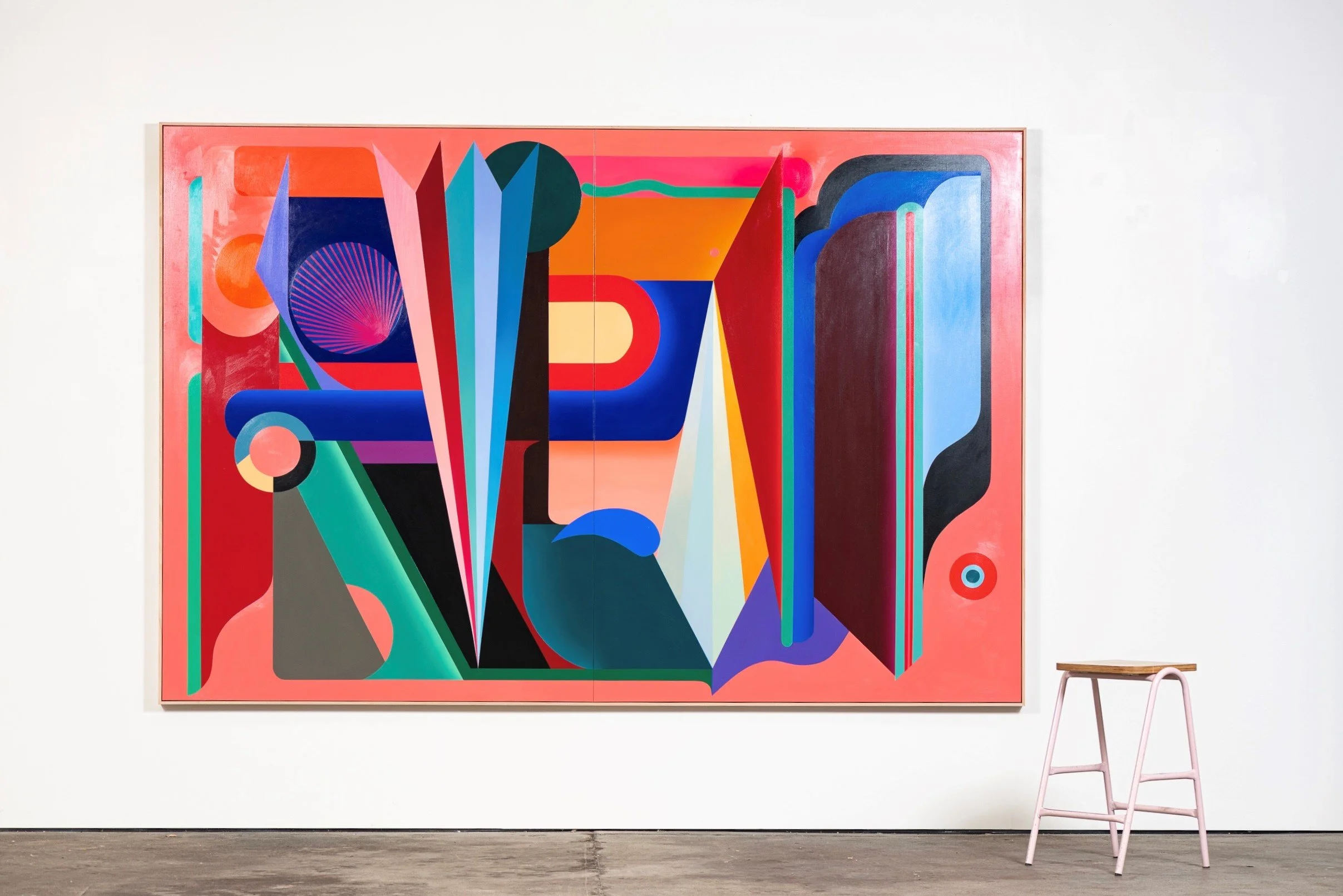 Colorful abstract geometric painting in an art gallery, with a wooden stool nearby.