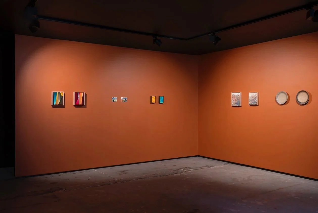 An art gallery with orange walls displays various small colorful paintings and plates.