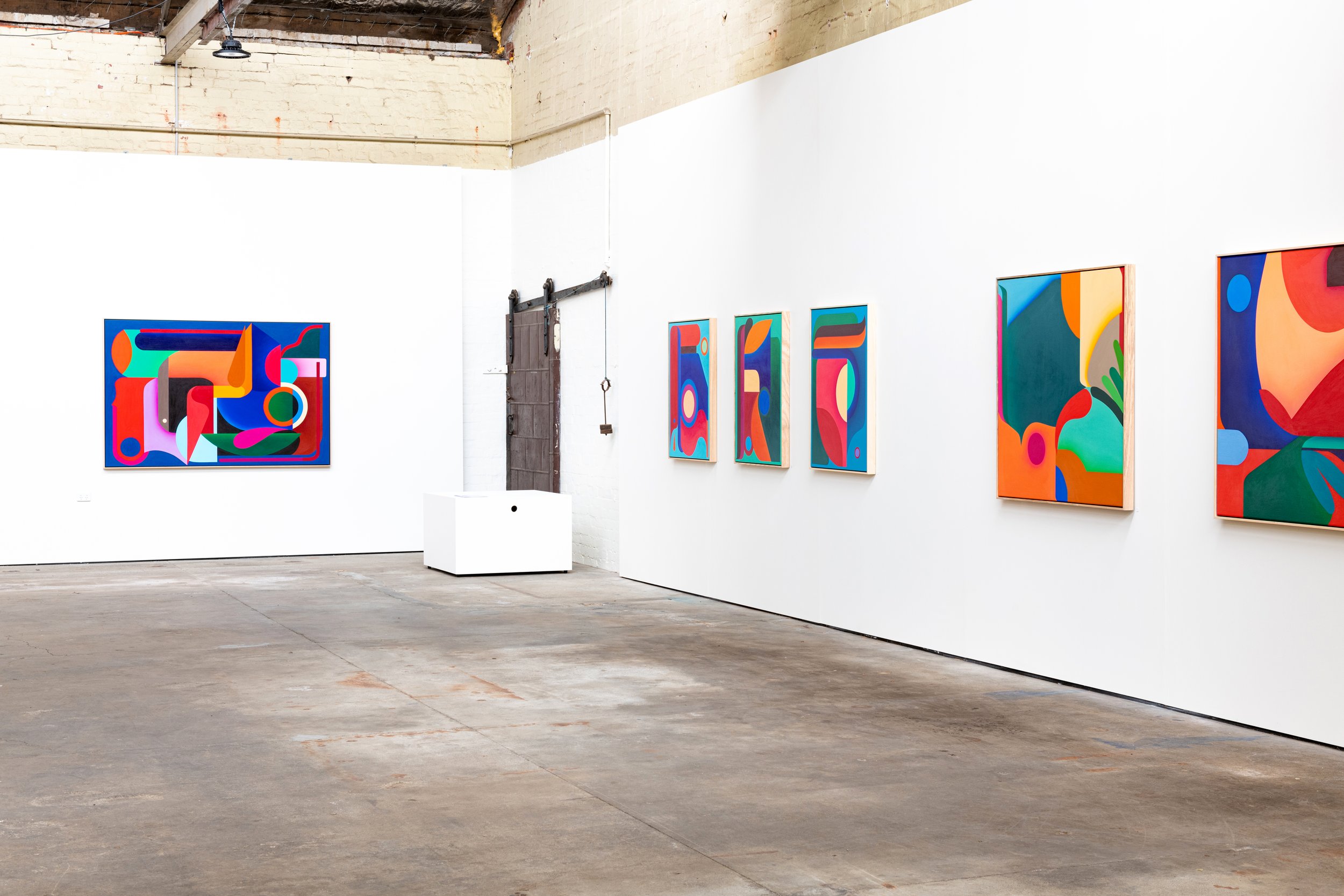 An art gallery with colorful abstract paintings on white walls, featuring geometric shapes and vibrant colors.
