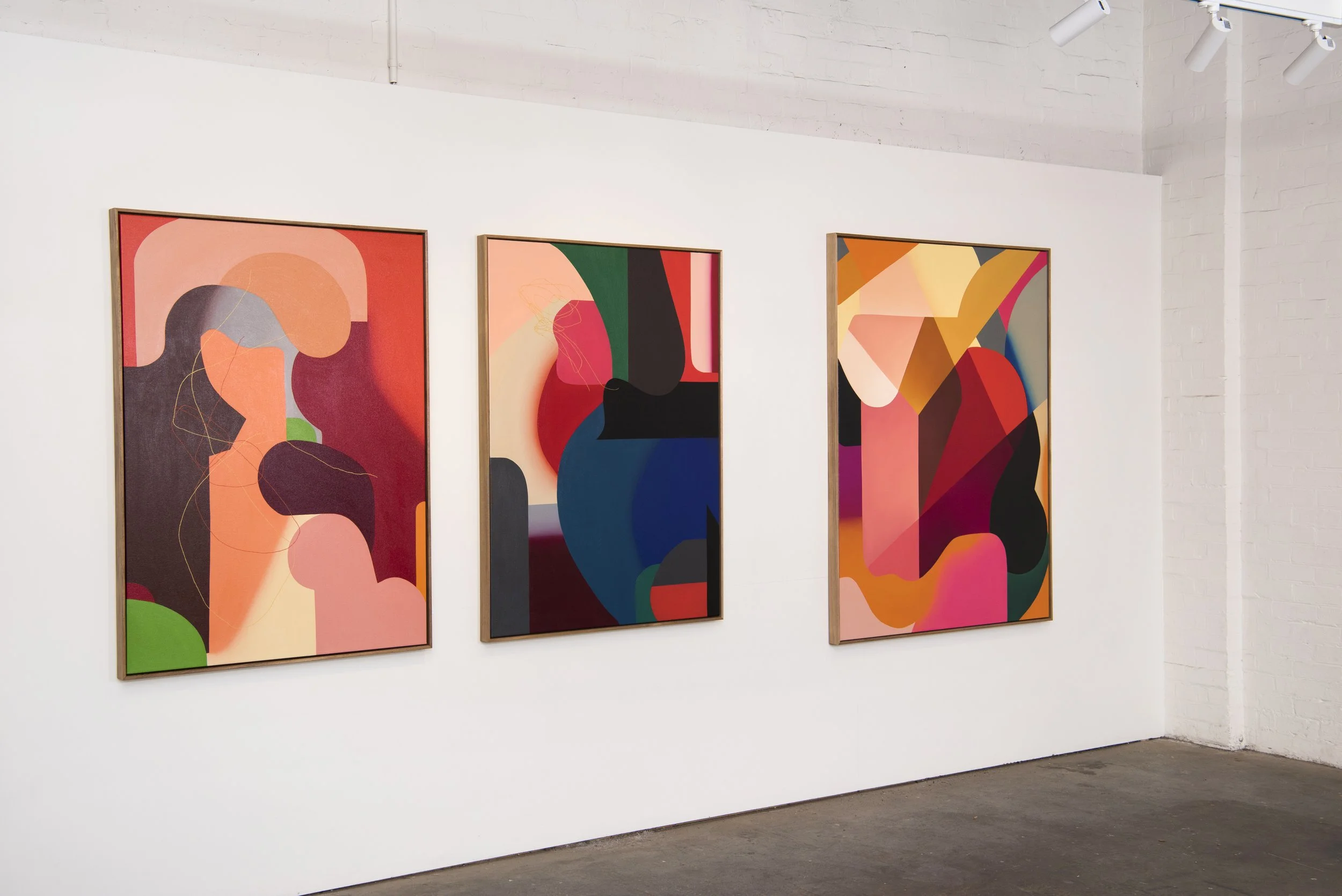Three colorful abstract paintings hanging on a white gallery wall.