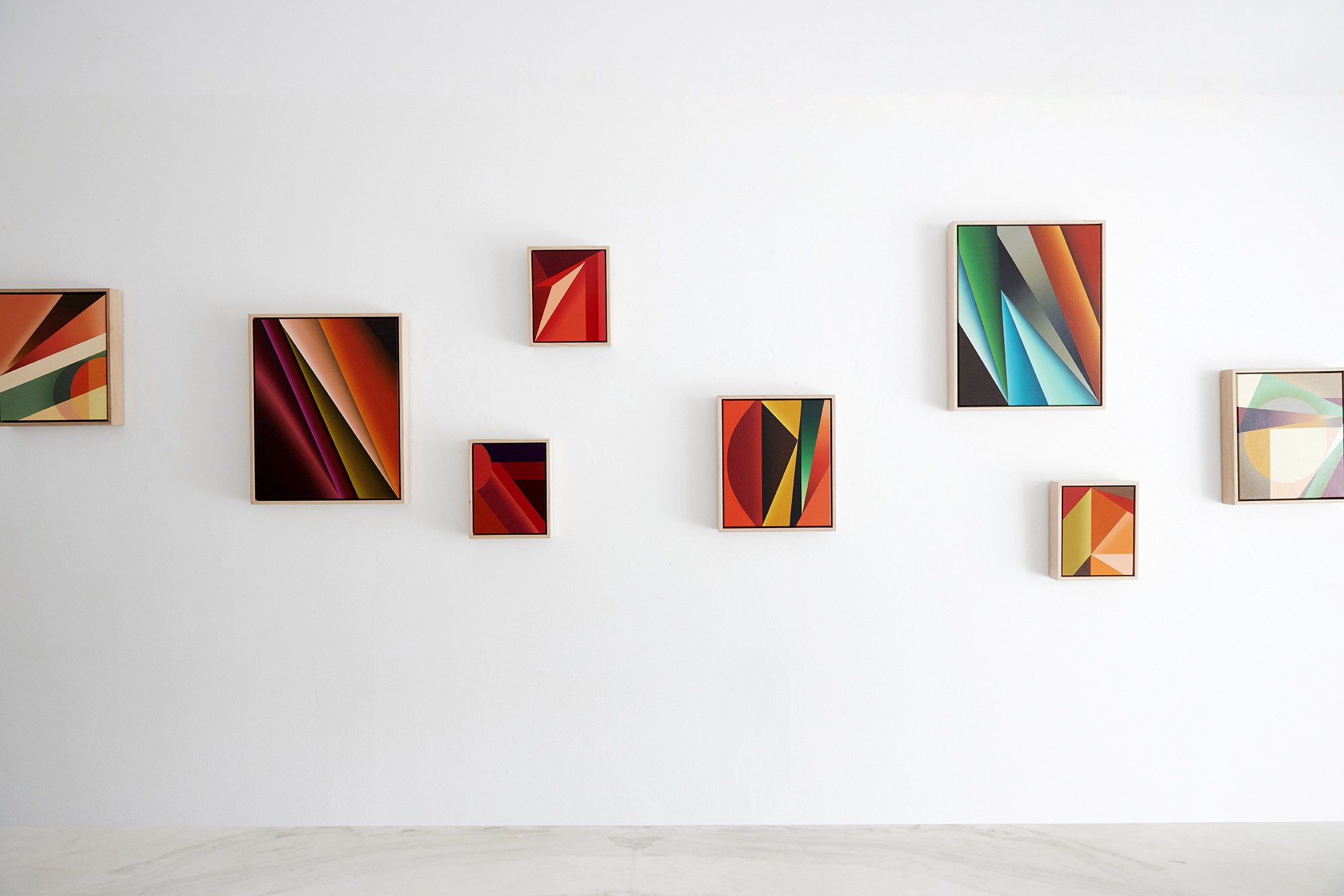 Gallery wall with abstract colorful paintings in frames, arranged on a white wall.