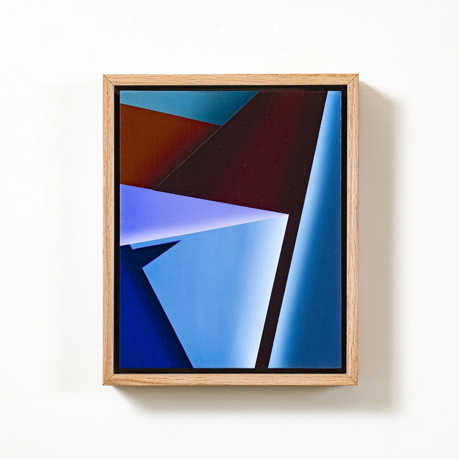 Abstract modern art piece with geometric shapes in shades of blue, black, and red, framed in wood and mounted on a white wall.