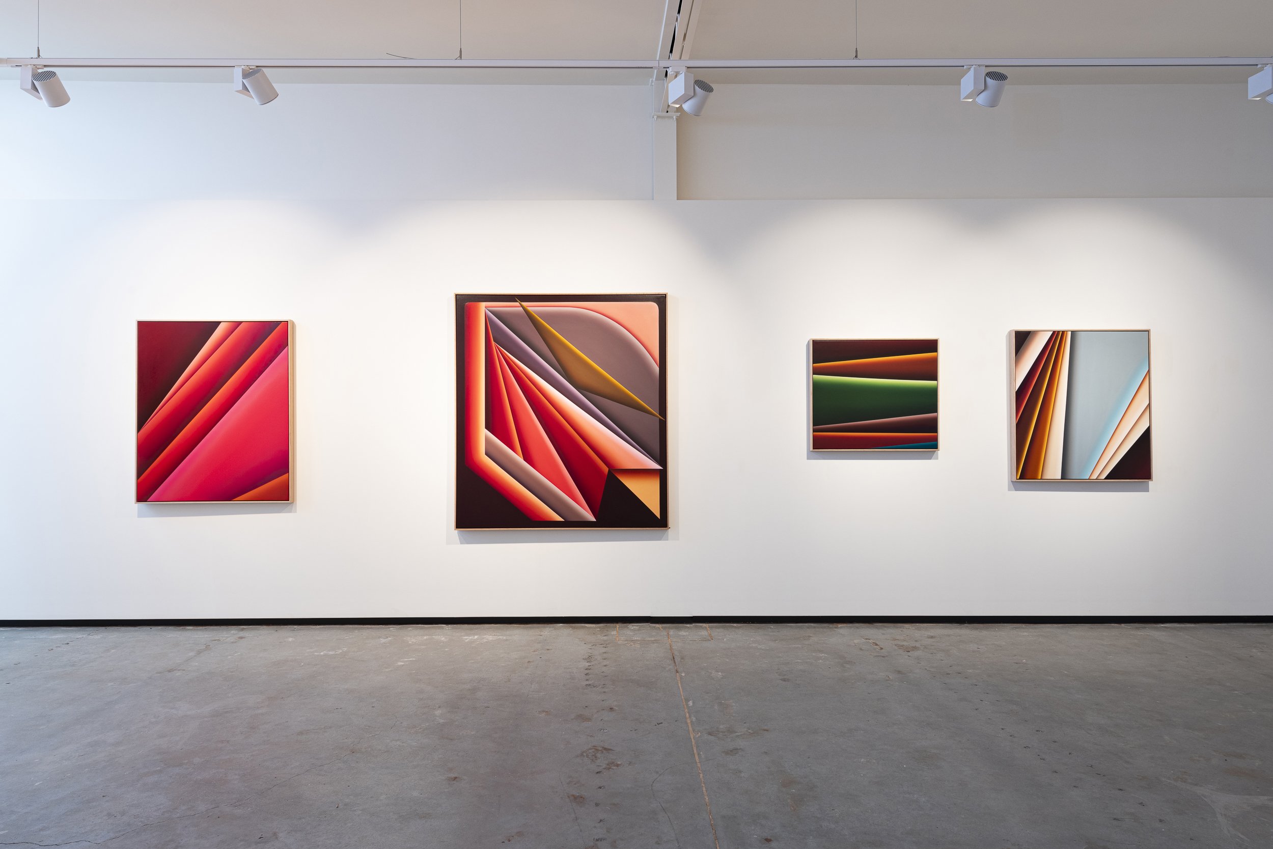 Art gallery wall displaying four colorful abstract paintings with geometric shapes and vibrant shades of red, orange, green, and blue.