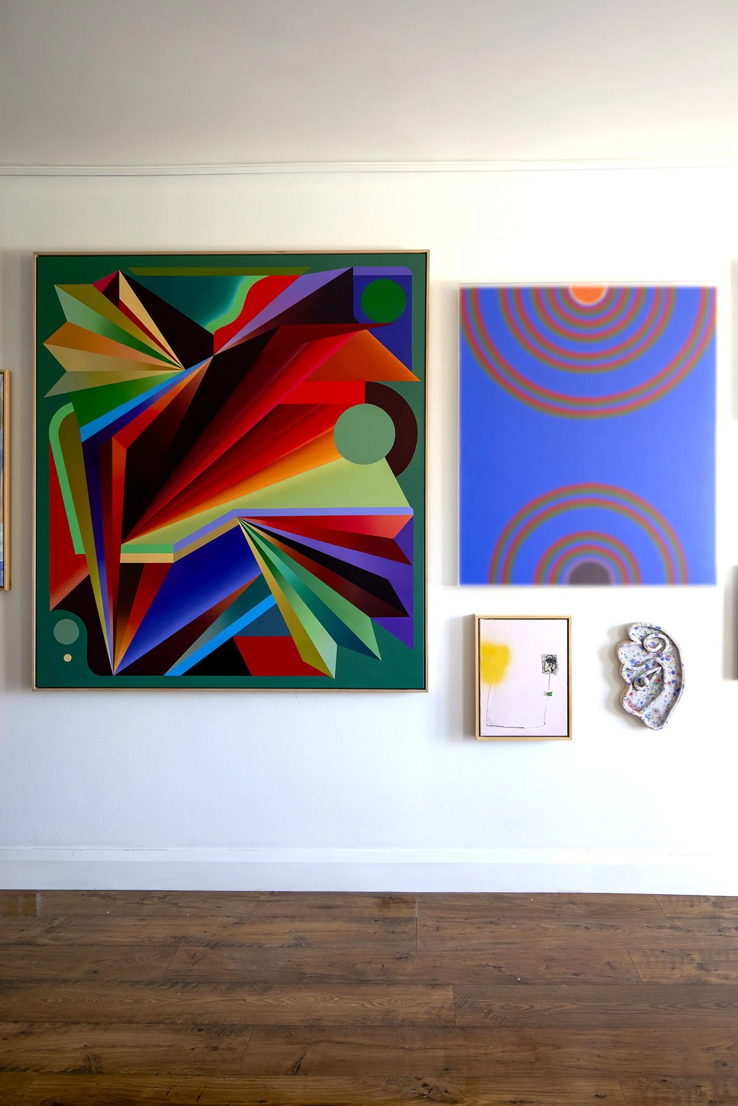Gallery wall with colorful abstract paintings and ceramic artwork on a white wall
